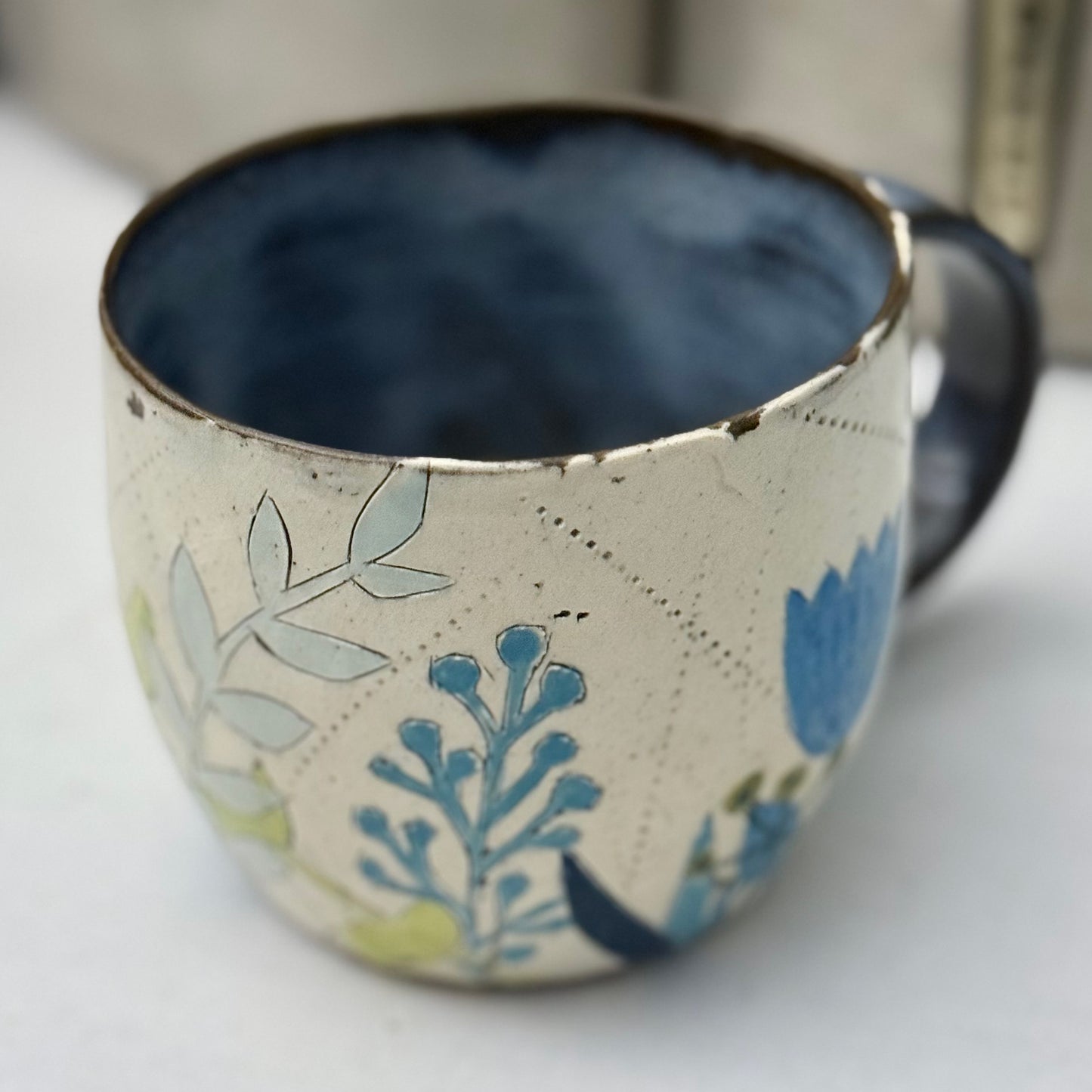 Ceramic mug with blue and green floral design on a white surface