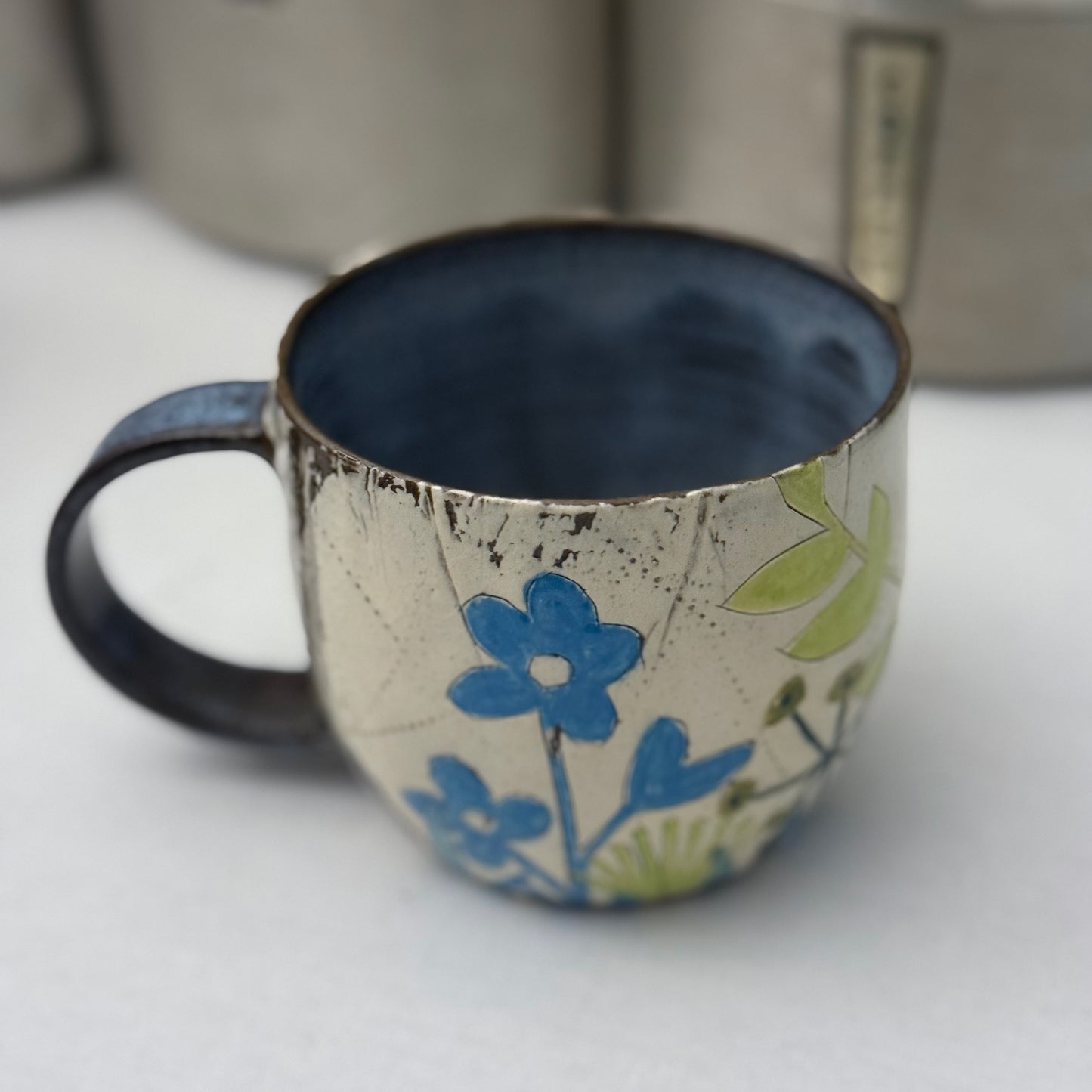 Ceramic mug with blue and green floral design on a white surface