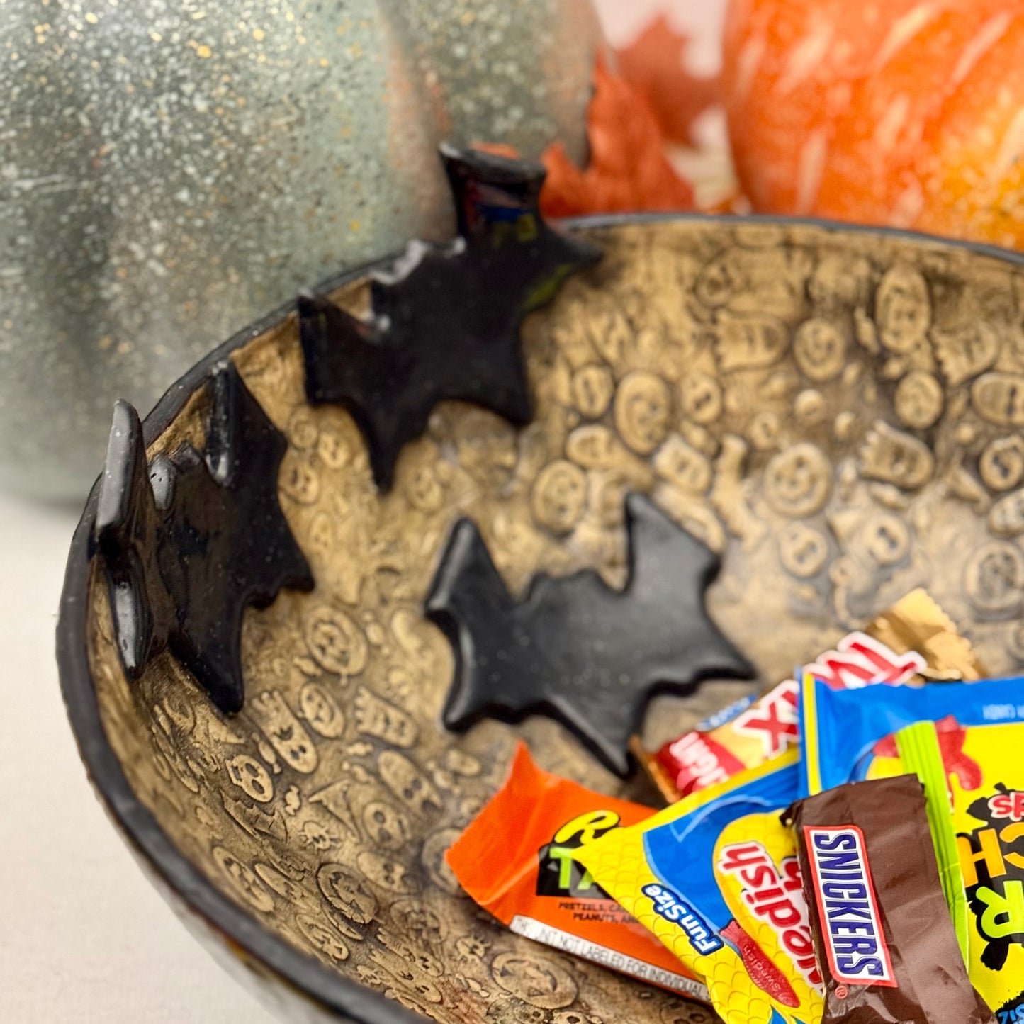 Ceramic candy bowl with halloween texture with bat accents on light background with pumpkins.