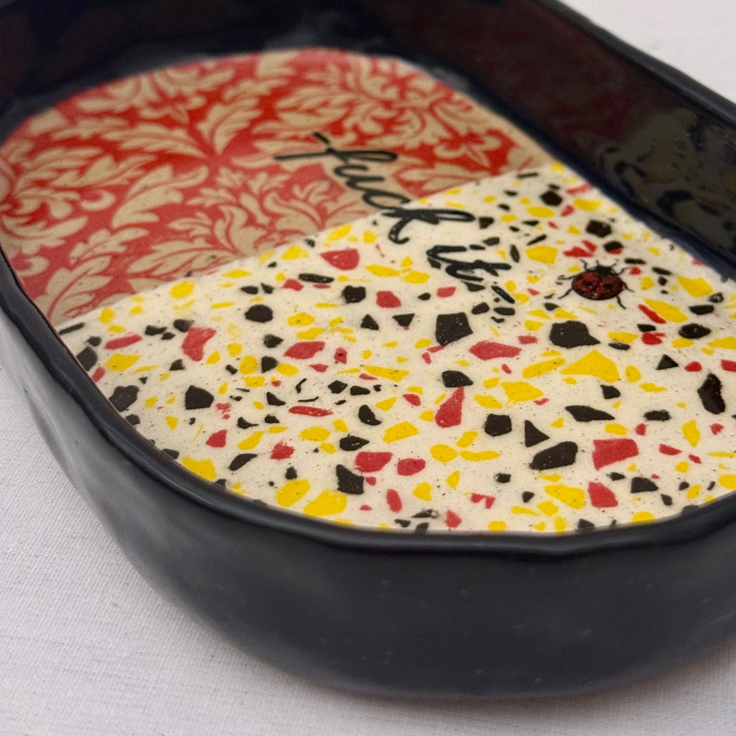 Decorative tray with damask pattern, black text, lady bug, and terrazzo design on a white background