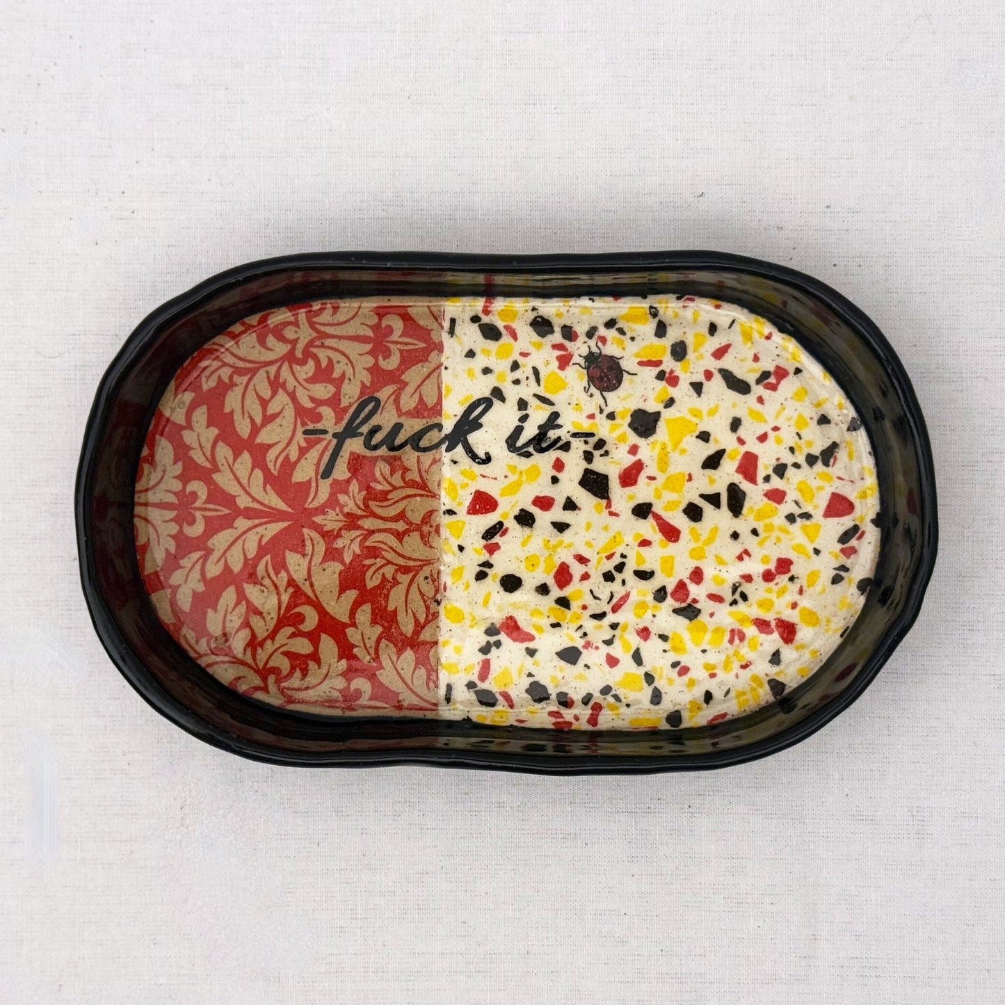 Decorative tray with damask pattern, black text, lady bug, and terrazzo design on a white background