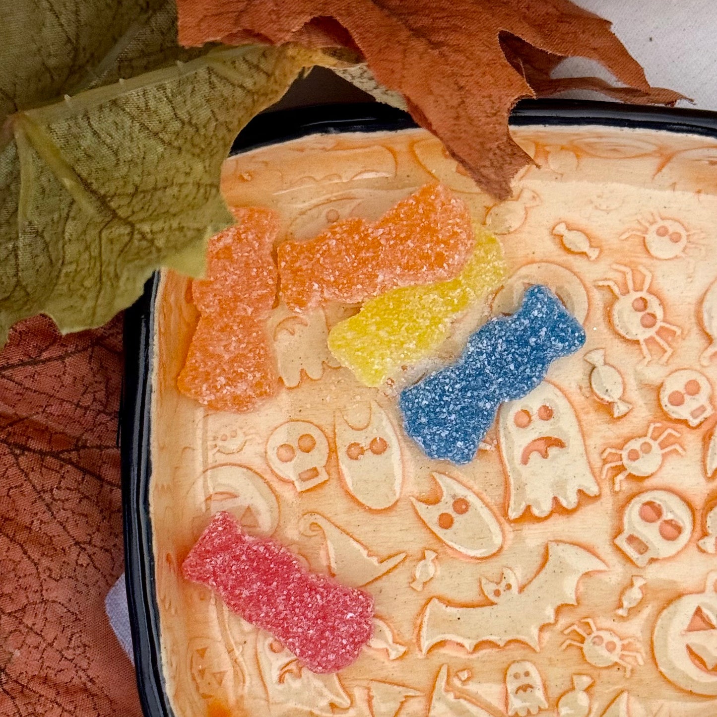 Macro view of decorative trinket dish with Halloween-themed design containing colorful gummy candy on a light background.