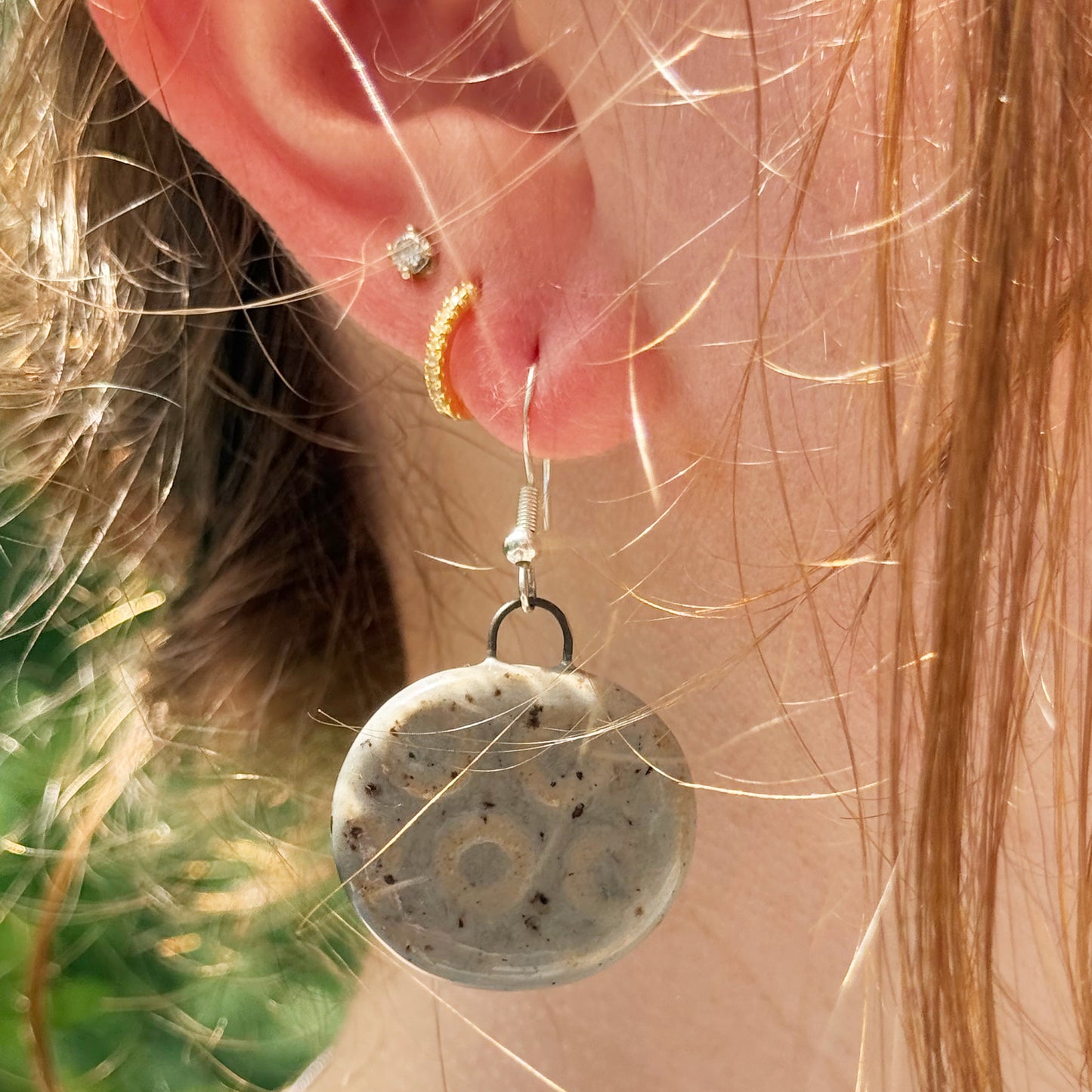 Close-up of a person wearing a round grey earring with a textured surface.