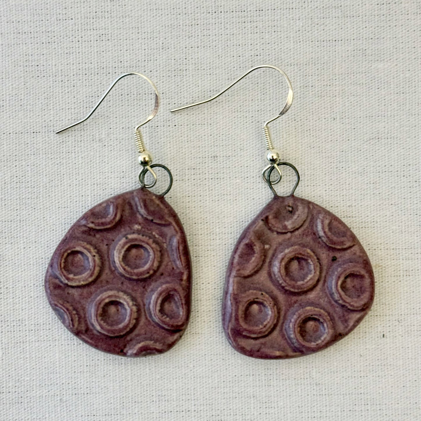 Pair of plum textured teardrop earrings on a light fabric background