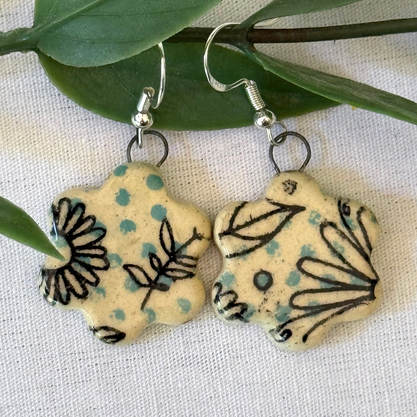 Pair of floral-patterned earrings on a white fabric background with green leaves.