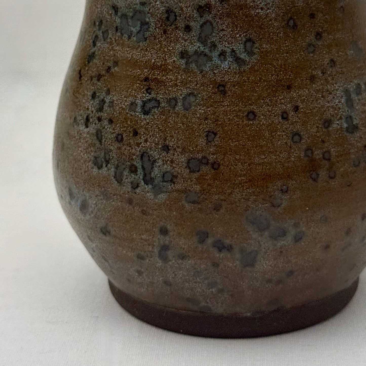 Close-up of a brown ceramic vase with speckled texture on a white background