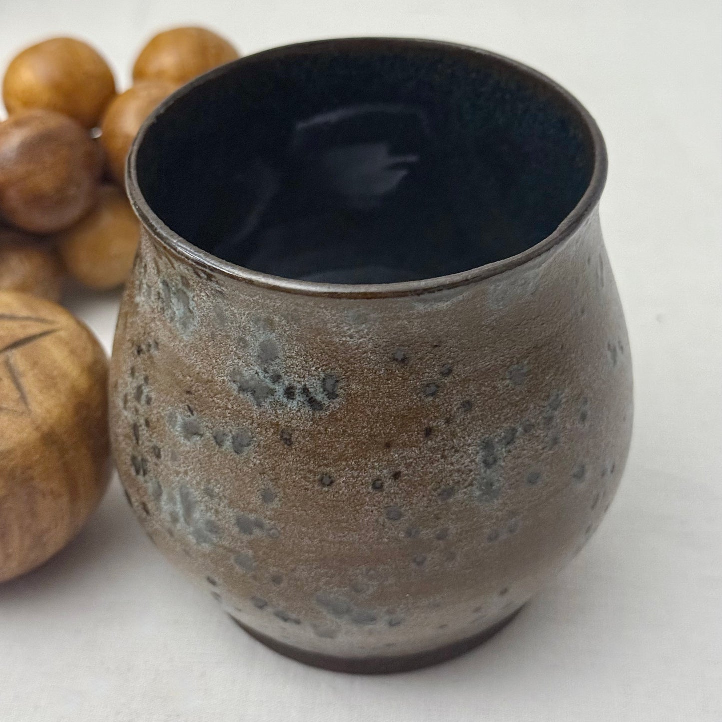 Ceramic cup with textured surface next to wooden fruit on a light background