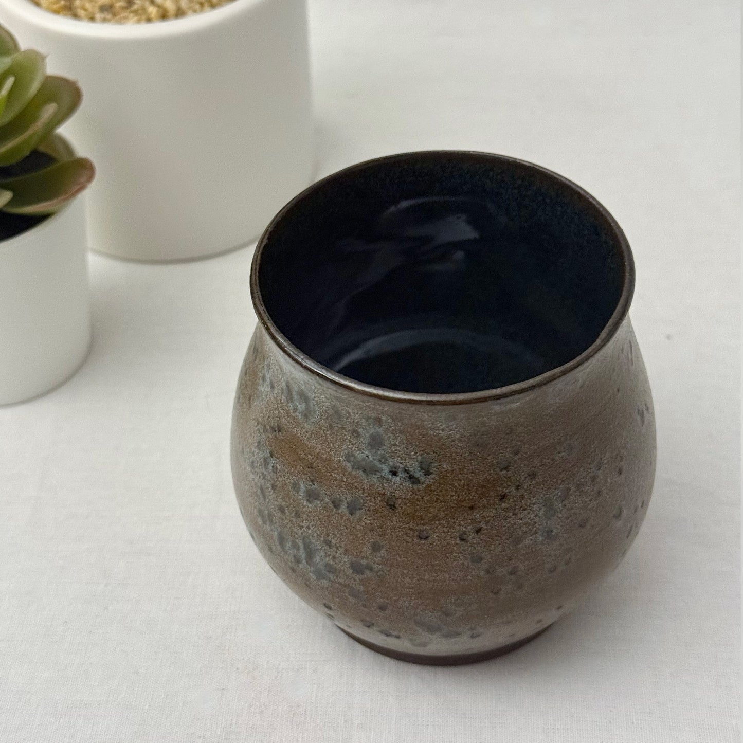 Ceramic cup with speckled design on a white surface with plants in the background