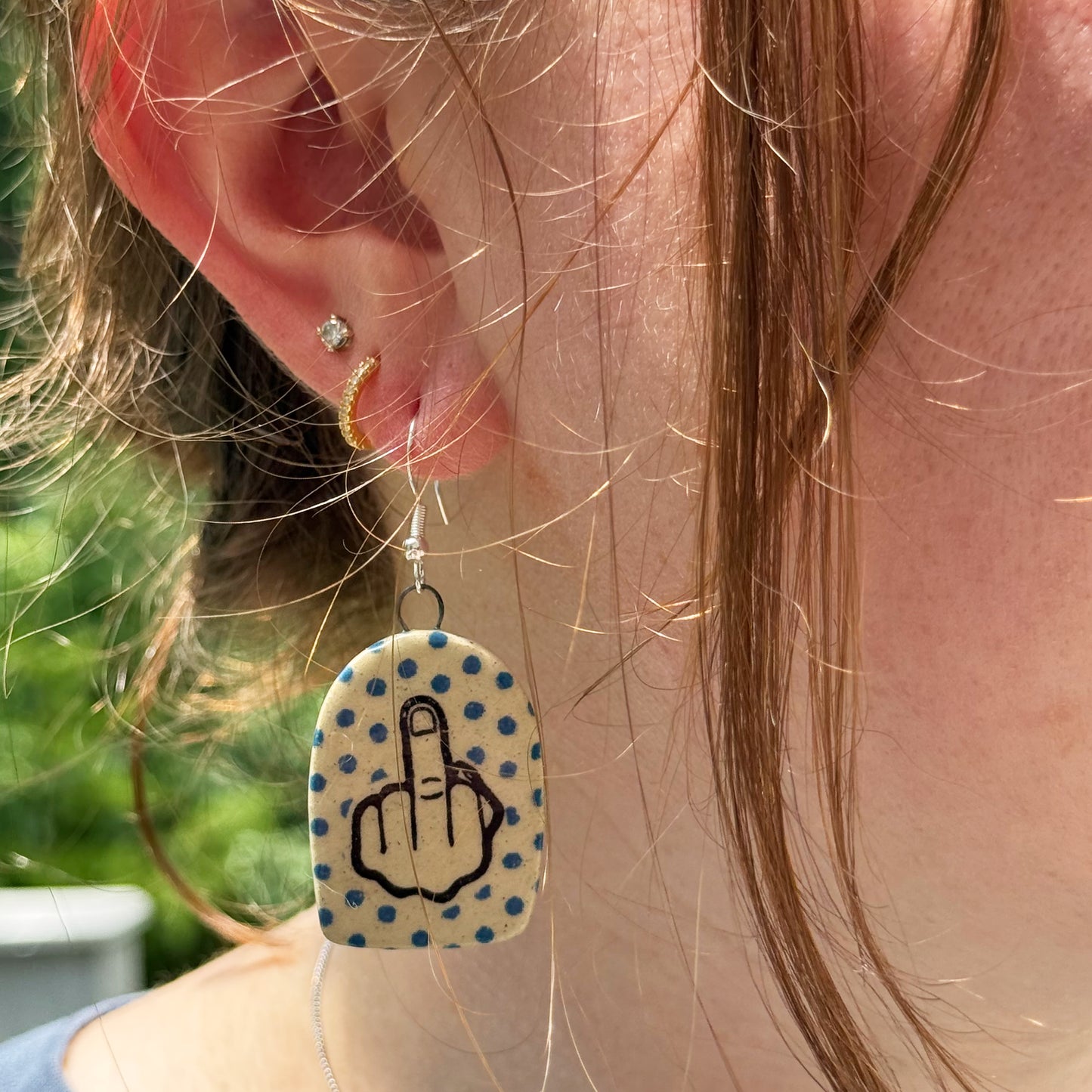 Earring with middle finger symbol on a polka dot background worn by a person.