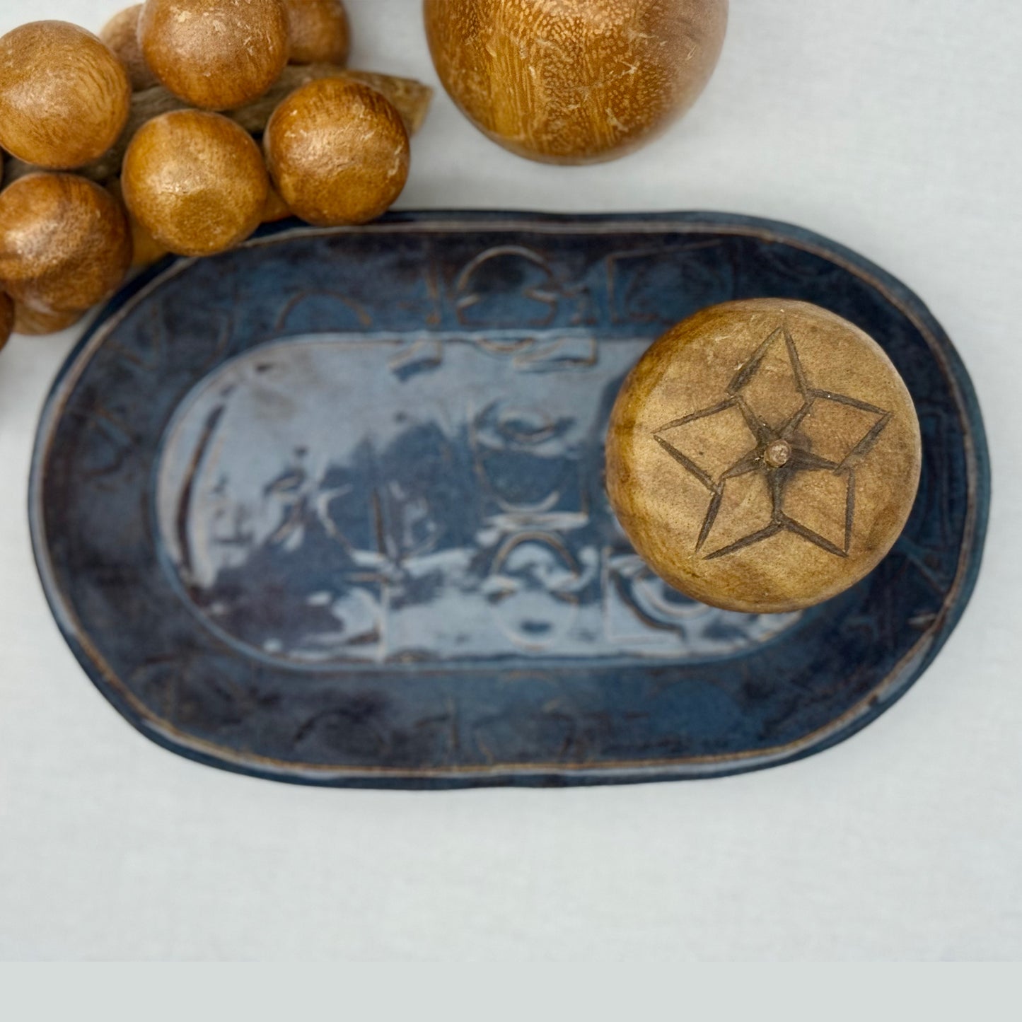 ceramic tray with mid century texture surrounded by monkey pod wooden fruit on a light background