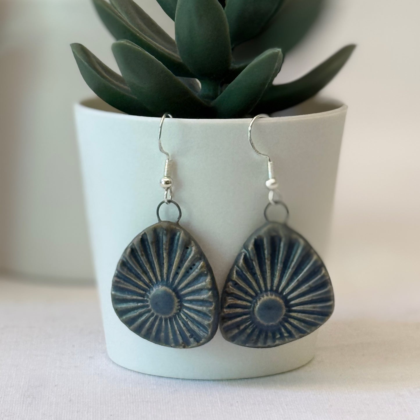 Earrings with sunburst design in a white pot with green plant