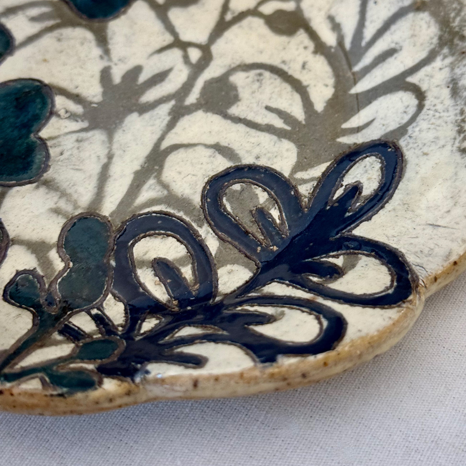 Ceramic plate with dark teal floral design on a white background