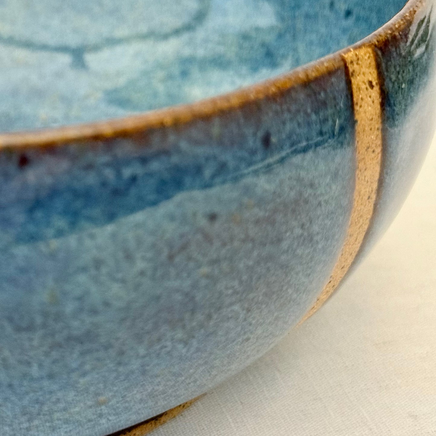 Close-up of a ceramic bowl with blue glaze and brown rim on a light background