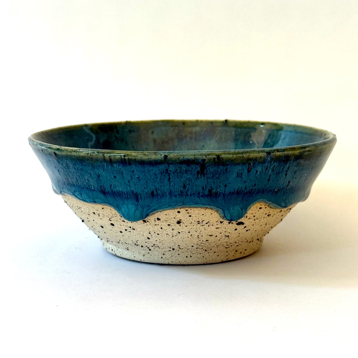 Handmade stoneware bowl with blue-green glaze interior and dripped glaze edge over a speckled clay base.