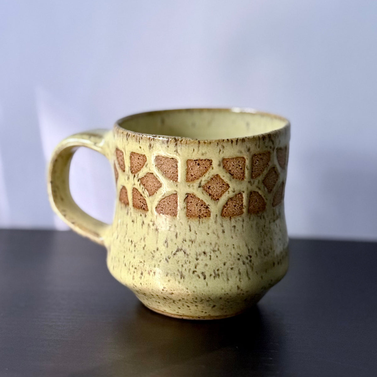 Handmade ceramic mug with a warm yellow glaze, featuring an empress breeze-block pattern around the upper half. The design reveals the natural clay beneath, giving the mug a retro mid-century architectural look.