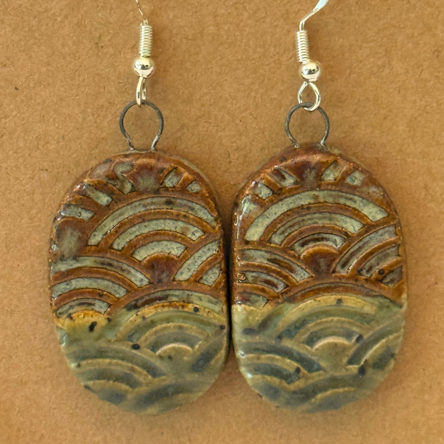Pair of ceramic earrings with wave pattern on a brown background