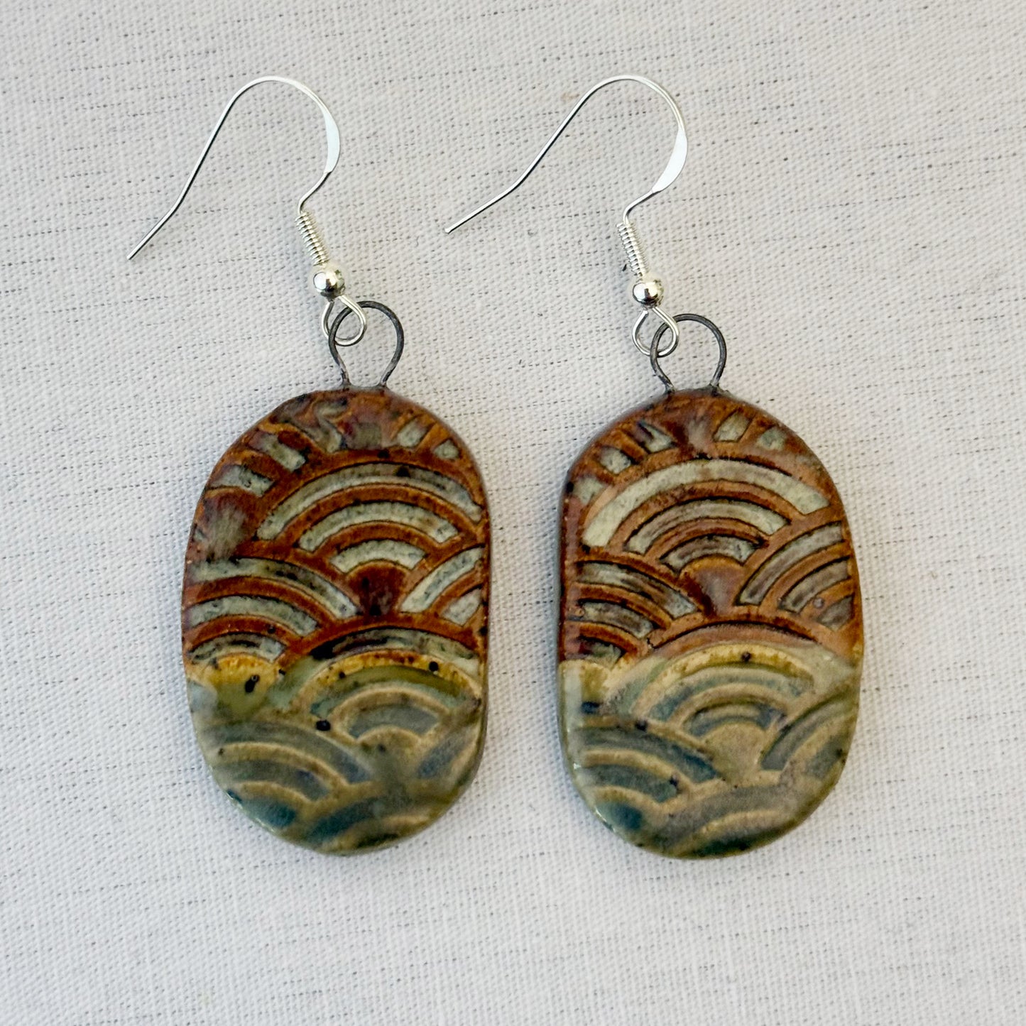 Pair of ceramic earrings with wave pattern on a light fabric background