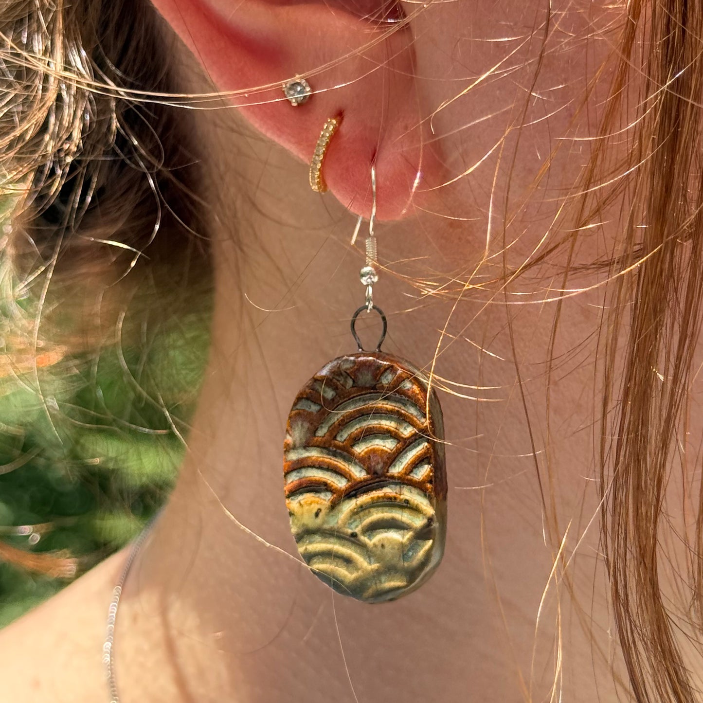 Close-up of a person wearing a textured earrings with a blurred natural background
