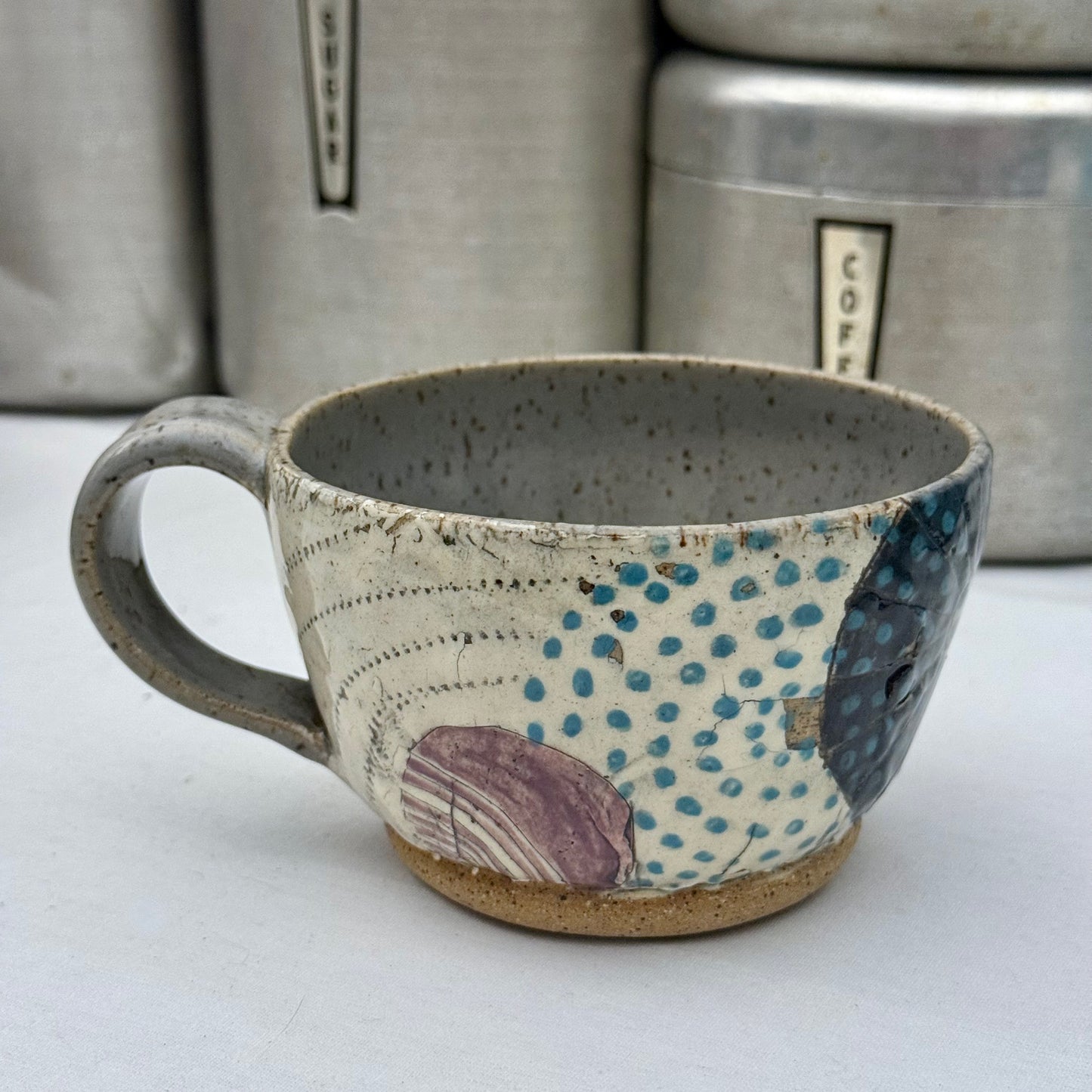 Handcrafted ceramic mug with textured surface and colorful patterns on a white background