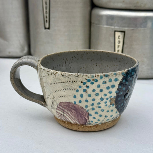 Handcrafted ceramic mug with textured surface and colorful patterns on a white background