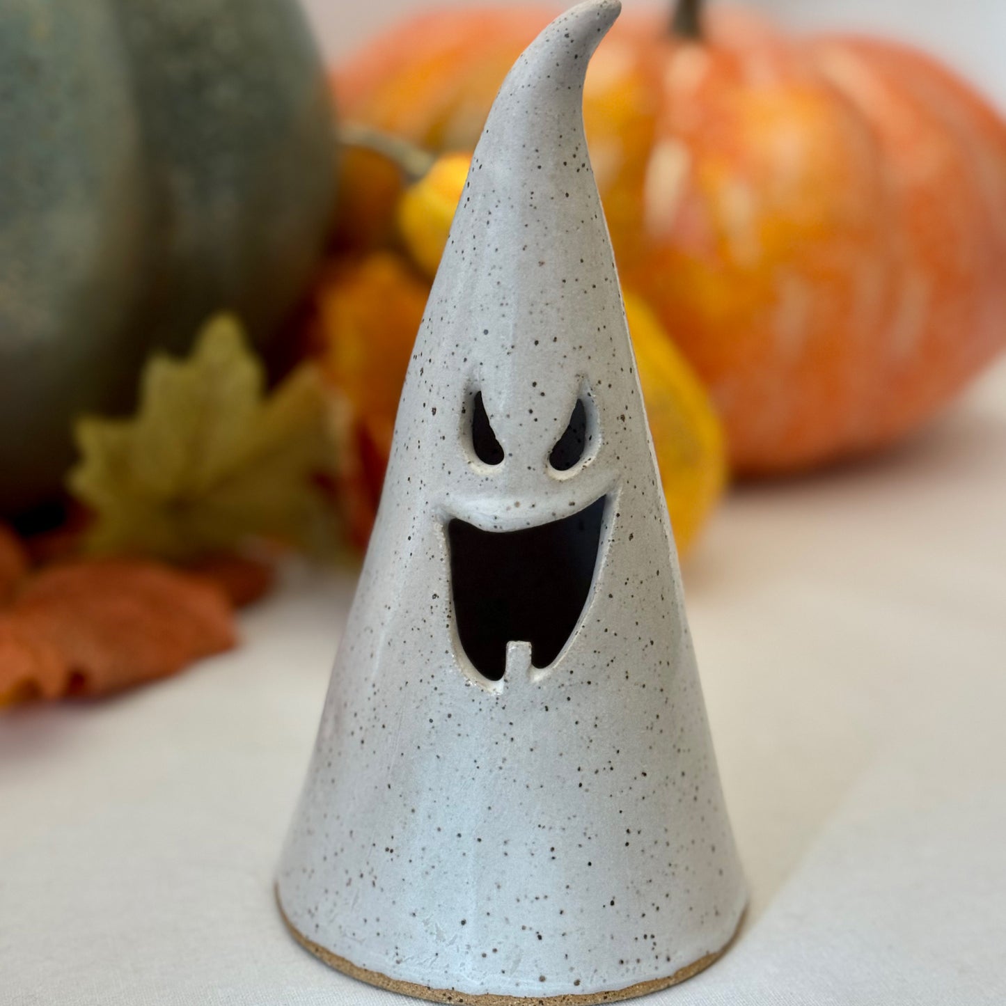 white ceramic ghost luminary with pumpkins and leaves in the background