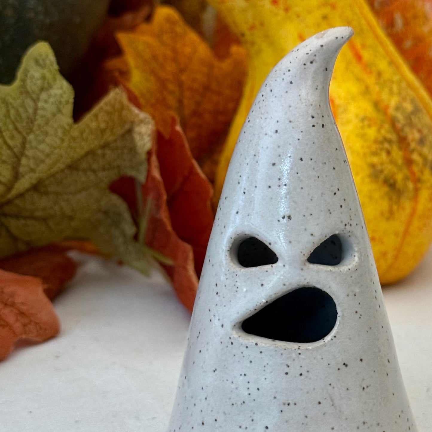 Ceramic luminary object on a white surface with autumn leaves and pumpkins in the background