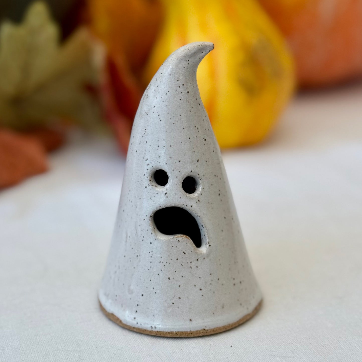 Ceramic ghost decoration with a surprised expression on a neutral background