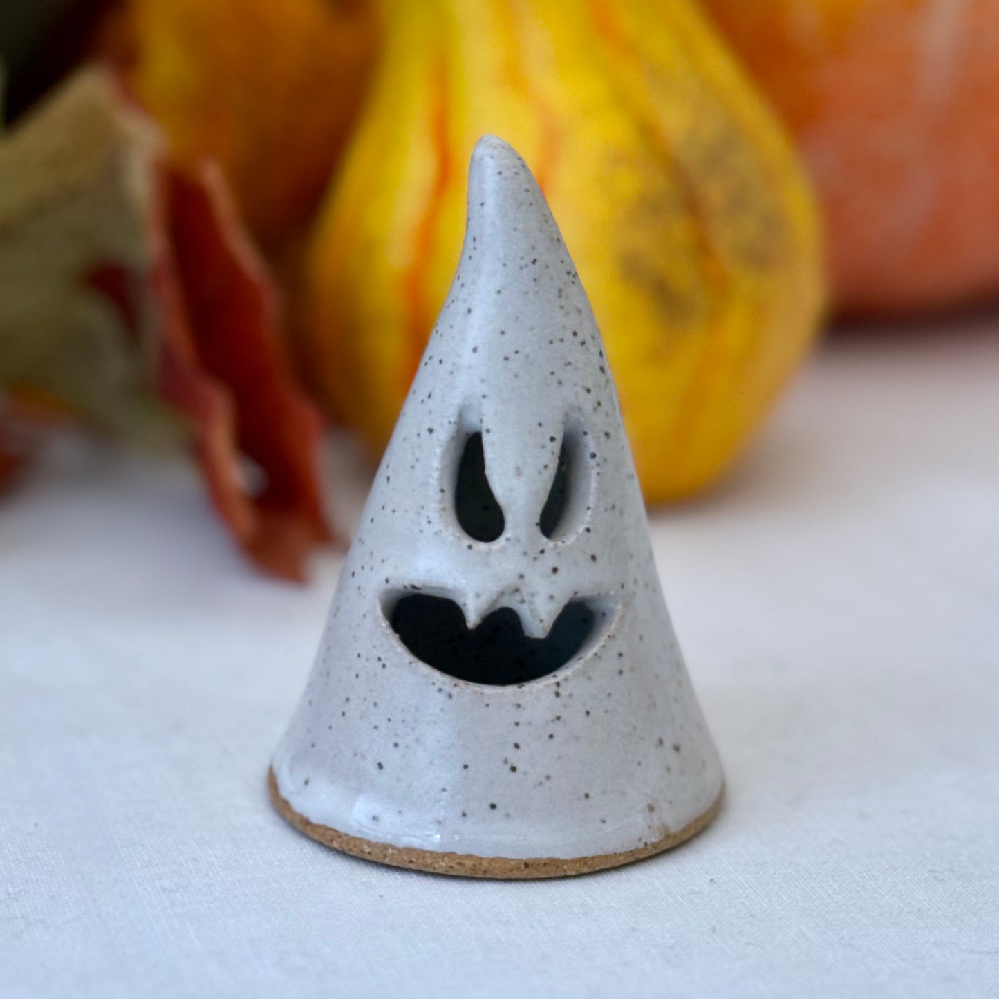 small Ceramic luminary on a white surface with pumpkins in the background