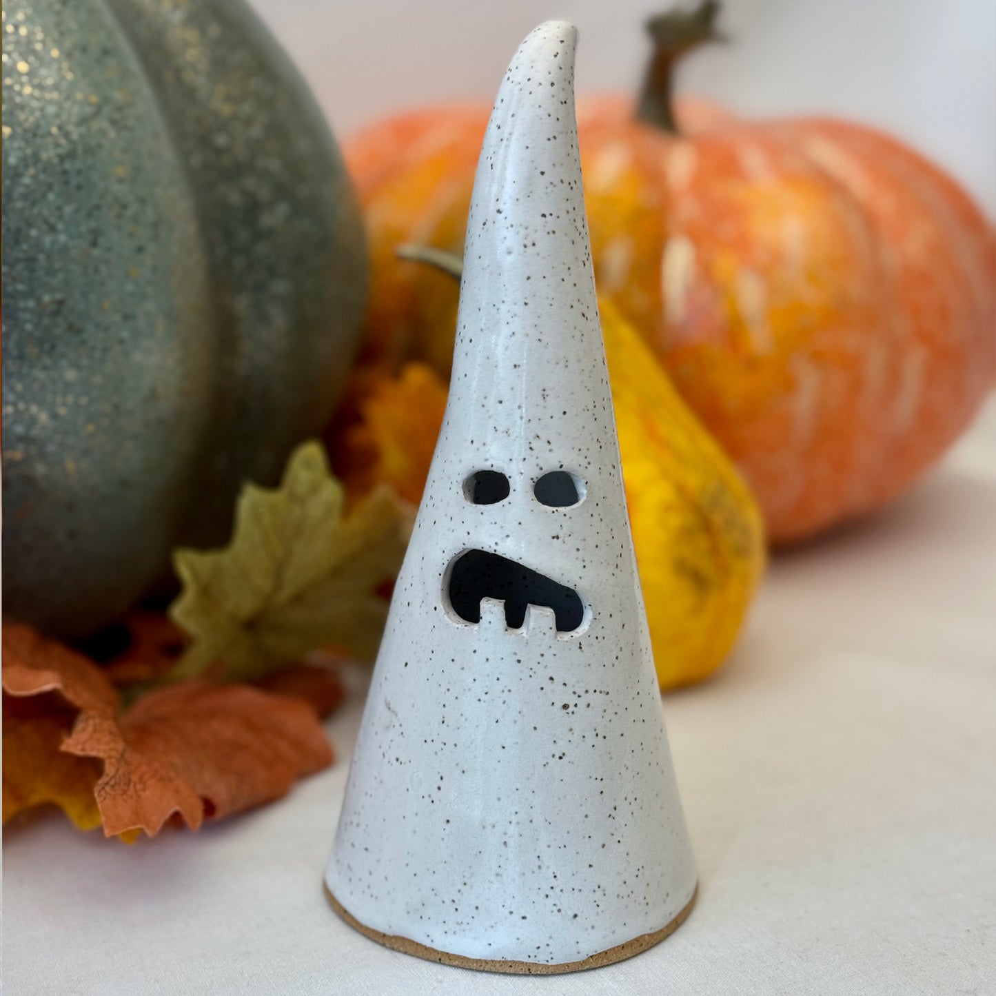 White ceramic luminary on a white surface with pumpkins and leaves in the background