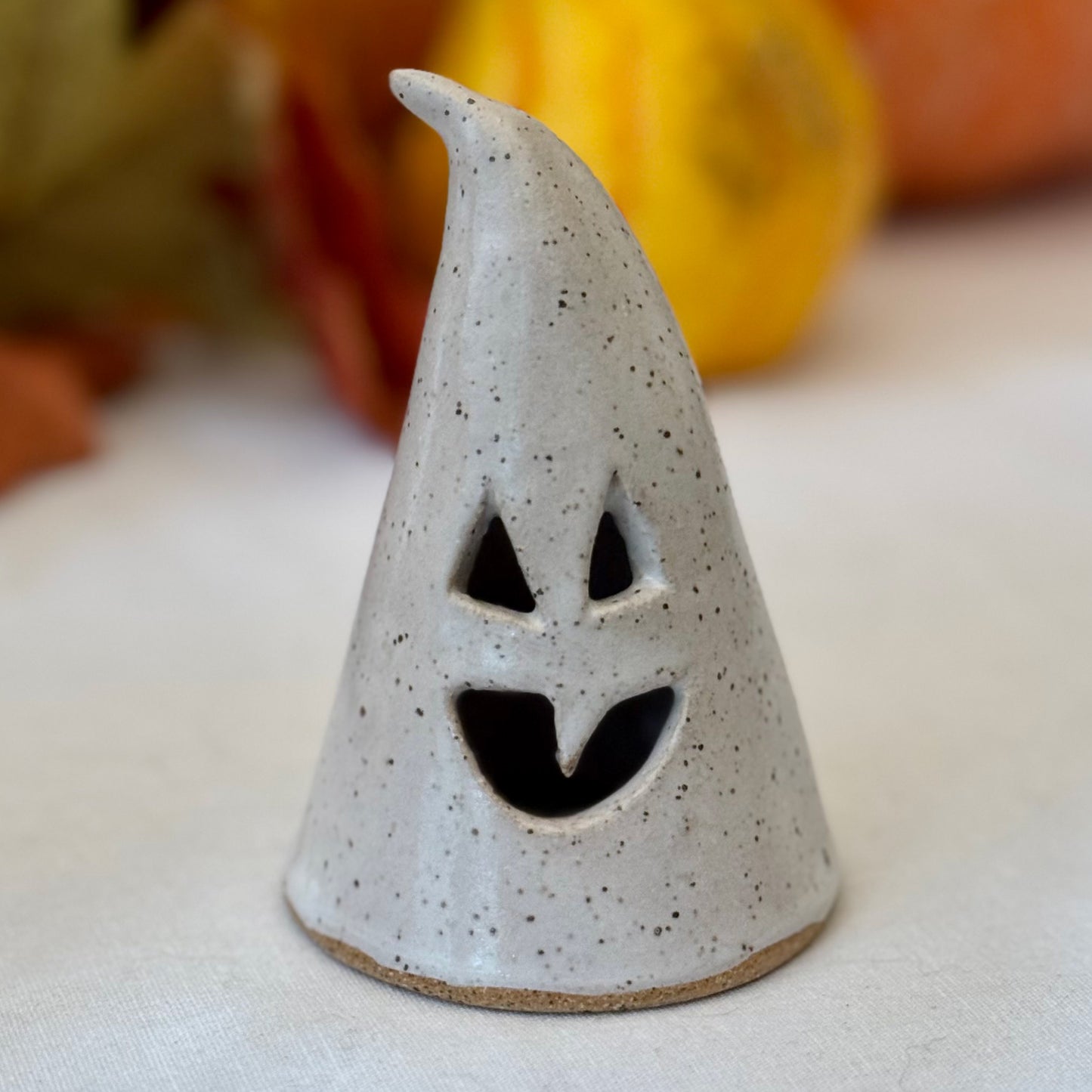 small ceramic luminary on a white surface with pumpkins in the background