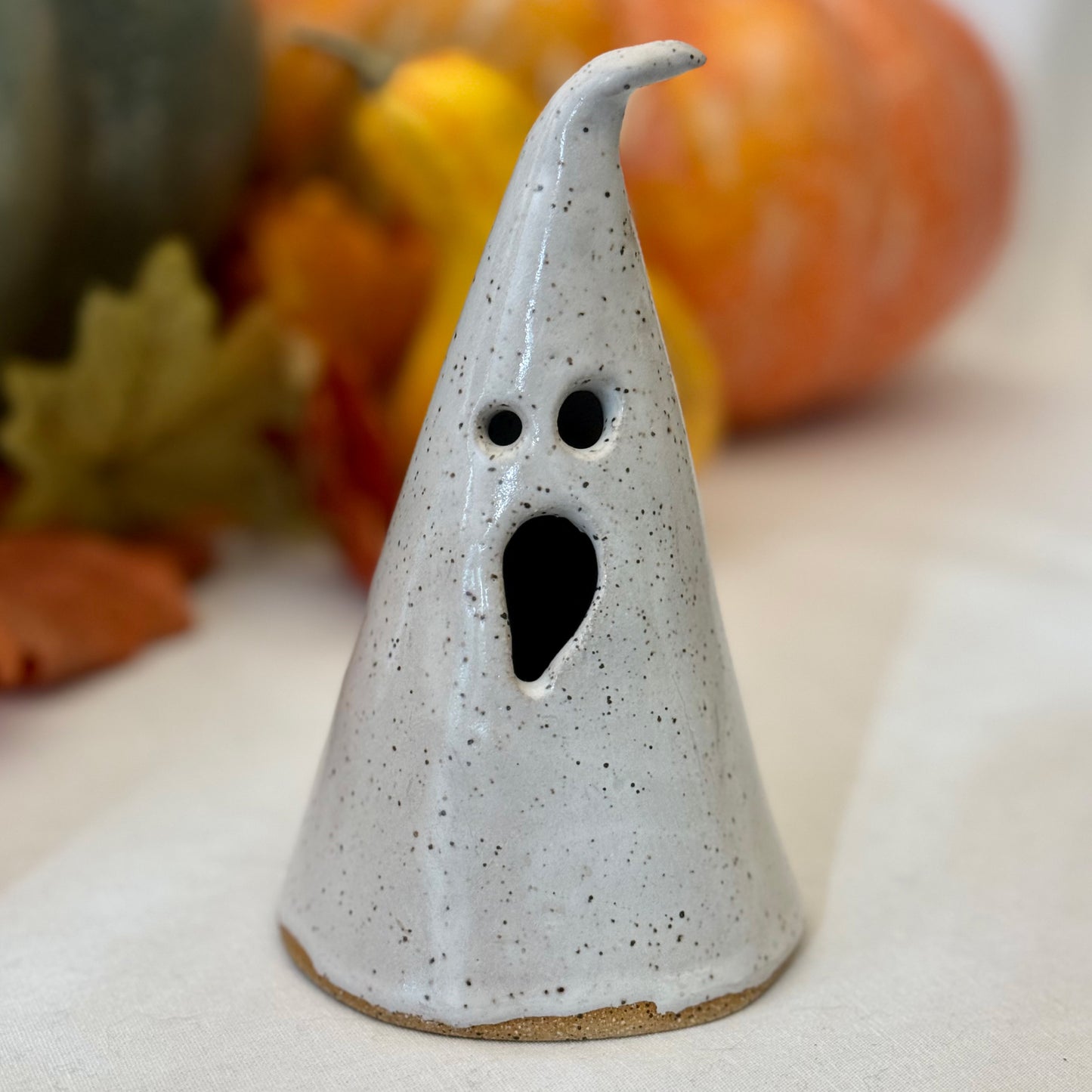 White ceramic ghost luminary on a white background with leaves and pumpkins
