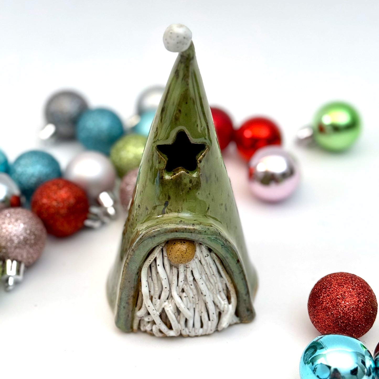 A ceramic gnome luminary with a green hat, star-shaped window, speckled white beard, and round nose, styled with Christmas ornaments.