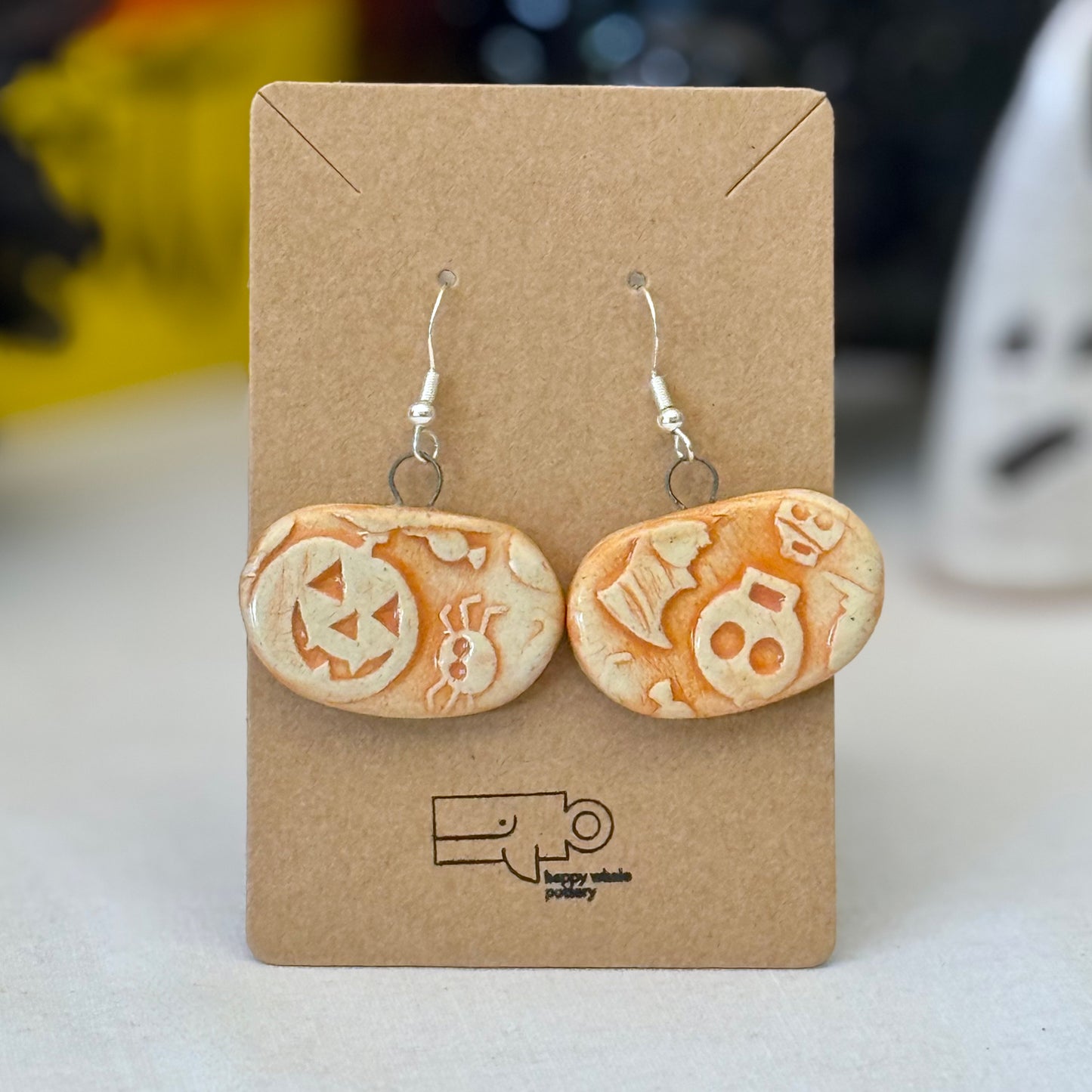 Pair of orange Halloween-themed earrings on a brown card with a blurred background
