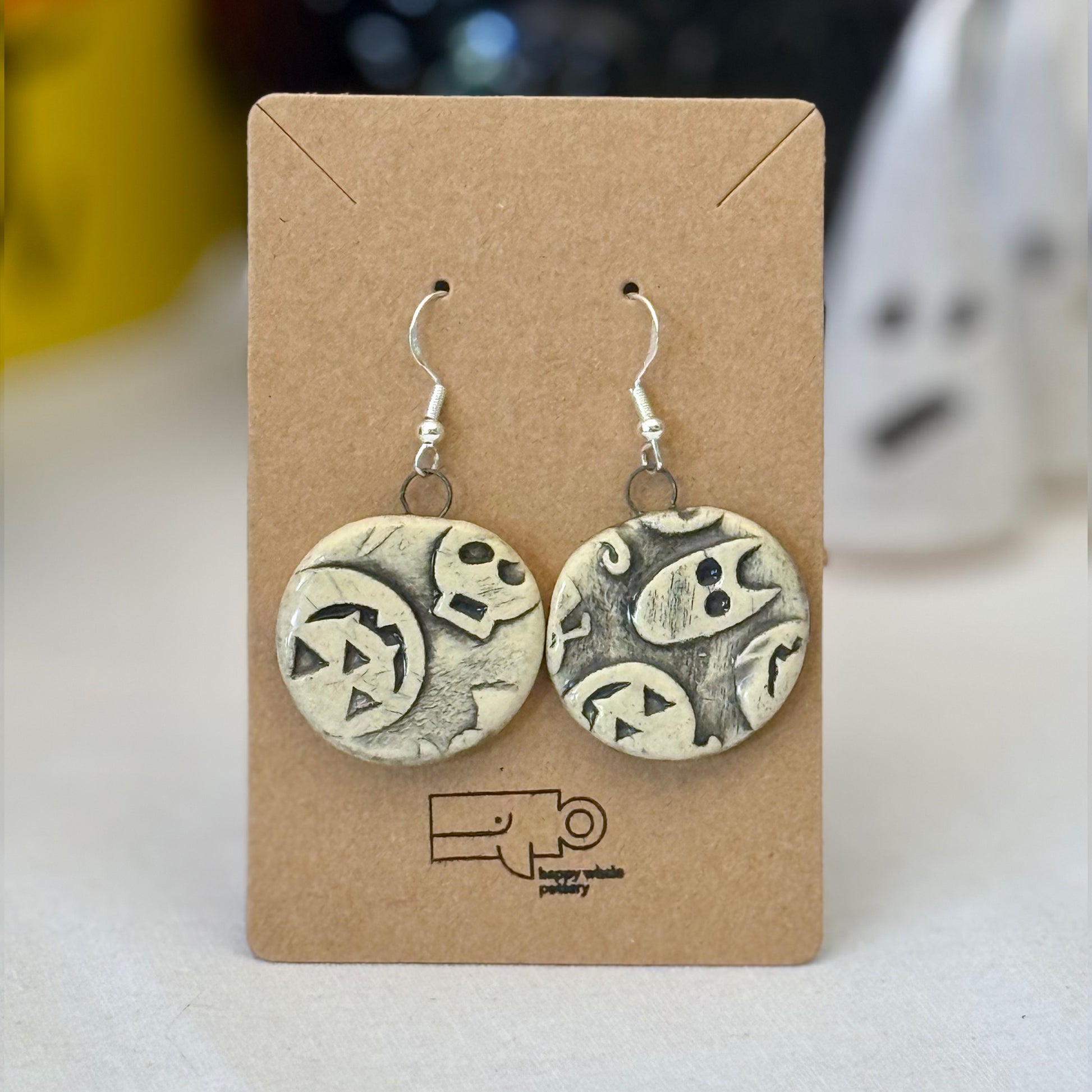 Pair of black halloween themed ceramic earrings on a brown card with a blurred background