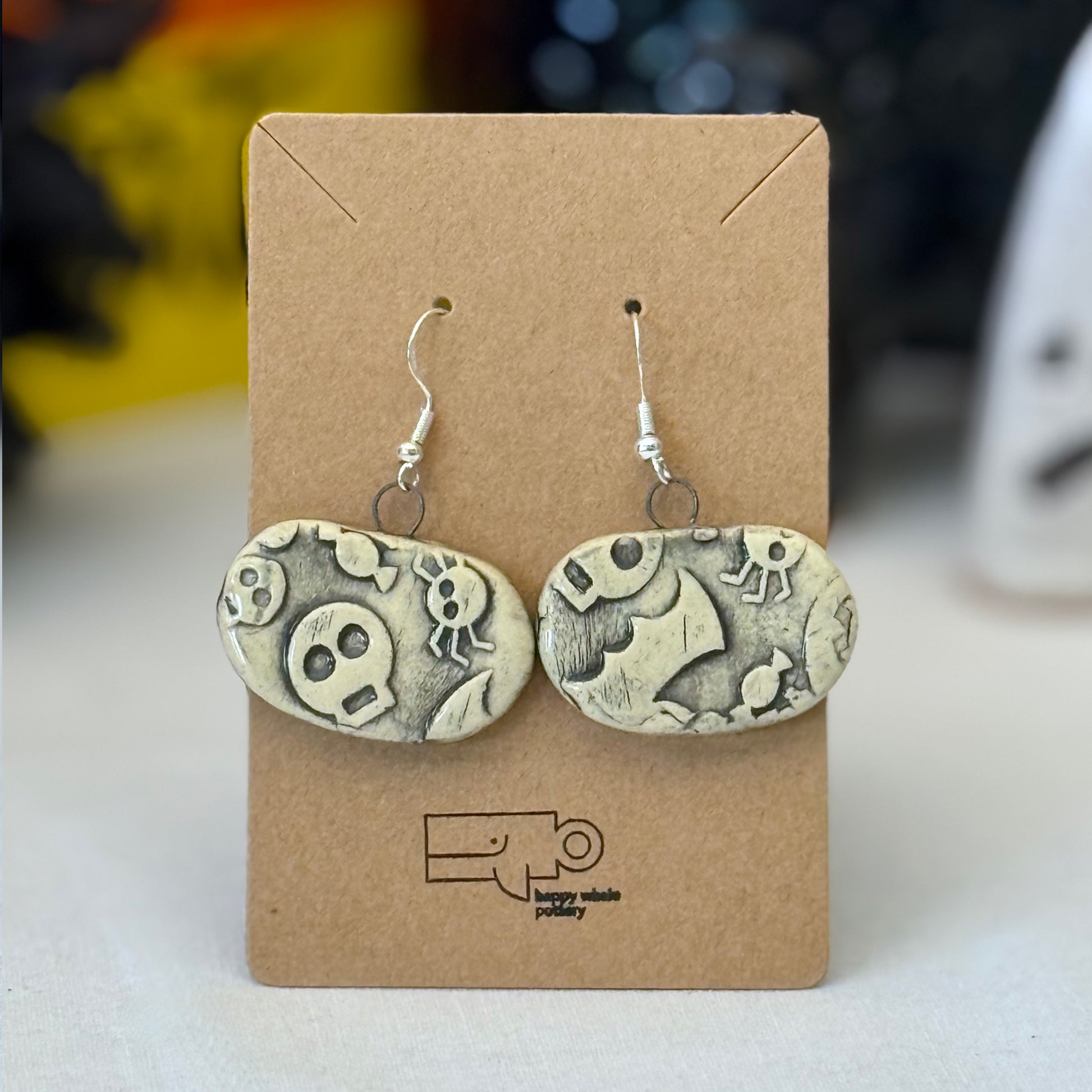 Pair of black halloween themed ceramic earrings on a brown card with a blurred background