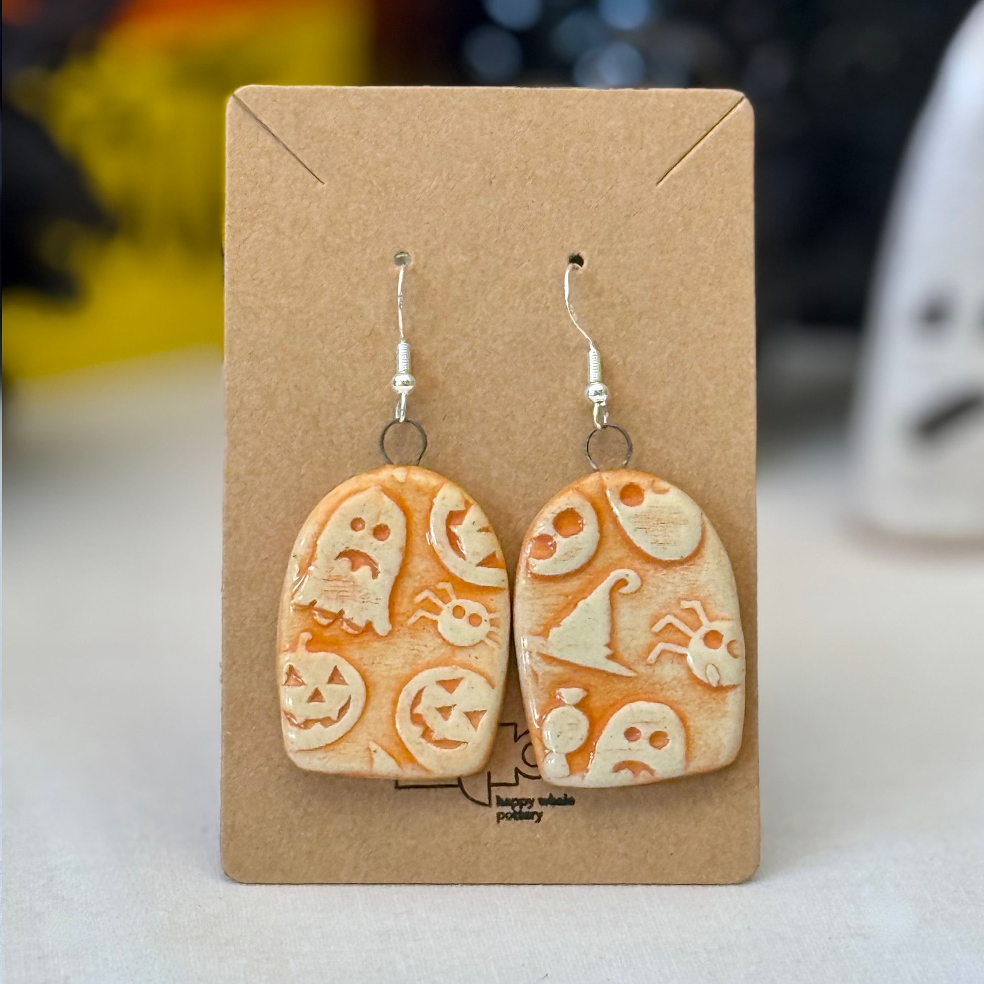 Pair of orange halloween themed ceramic earrings on a brown card with a blurred background