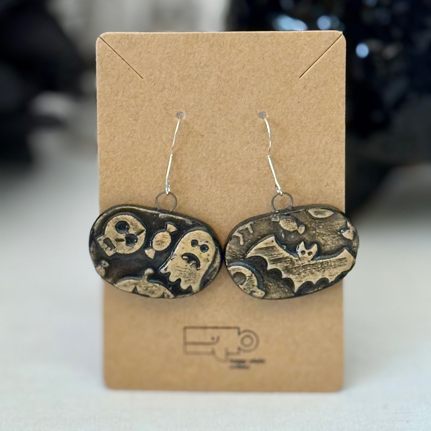 Pair of black and tan halloween themed ceramic earrings on a brown card with a blurred background