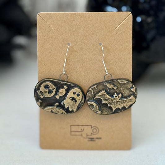 Pair of black and tan halloween themed ceramic earrings on a brown card with a blurred background