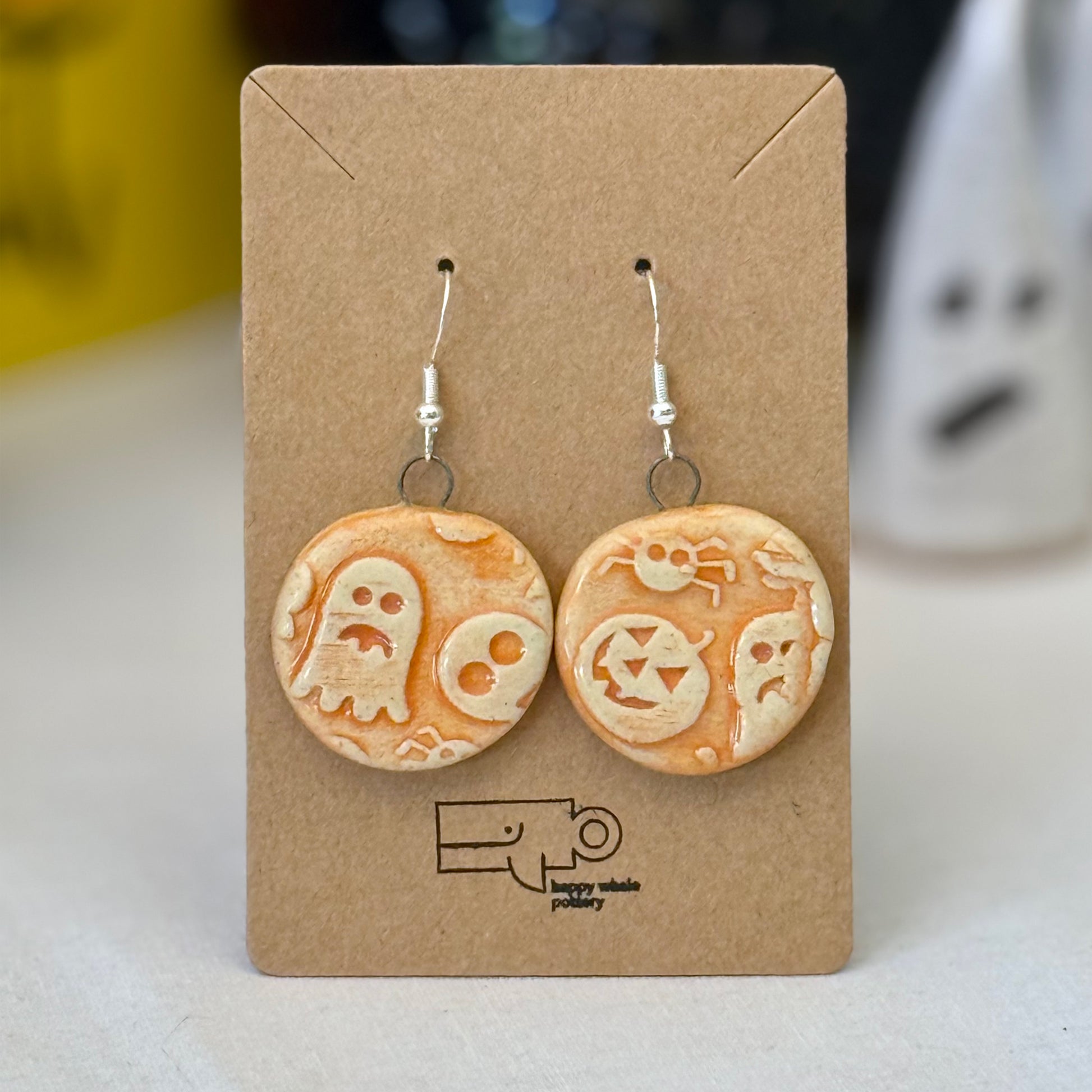Pair of orange halloween themed ceramic earrings on a brown card with a blurred background