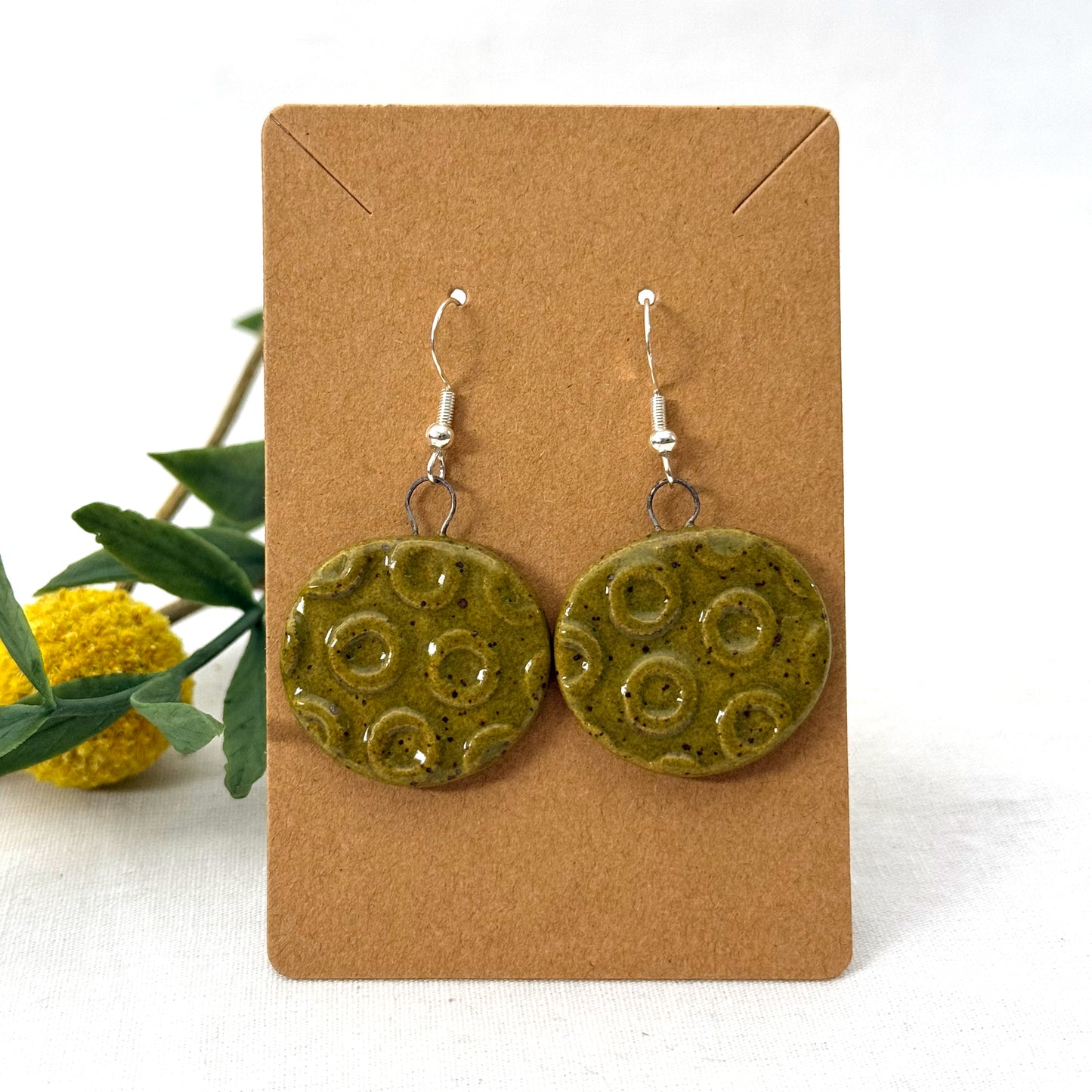 Green ceramic earrings on a brown card with a white background