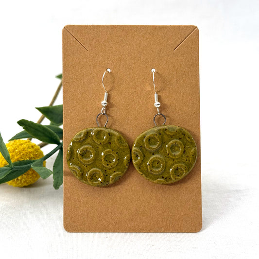 Green ceramic earrings on a brown card with a white background