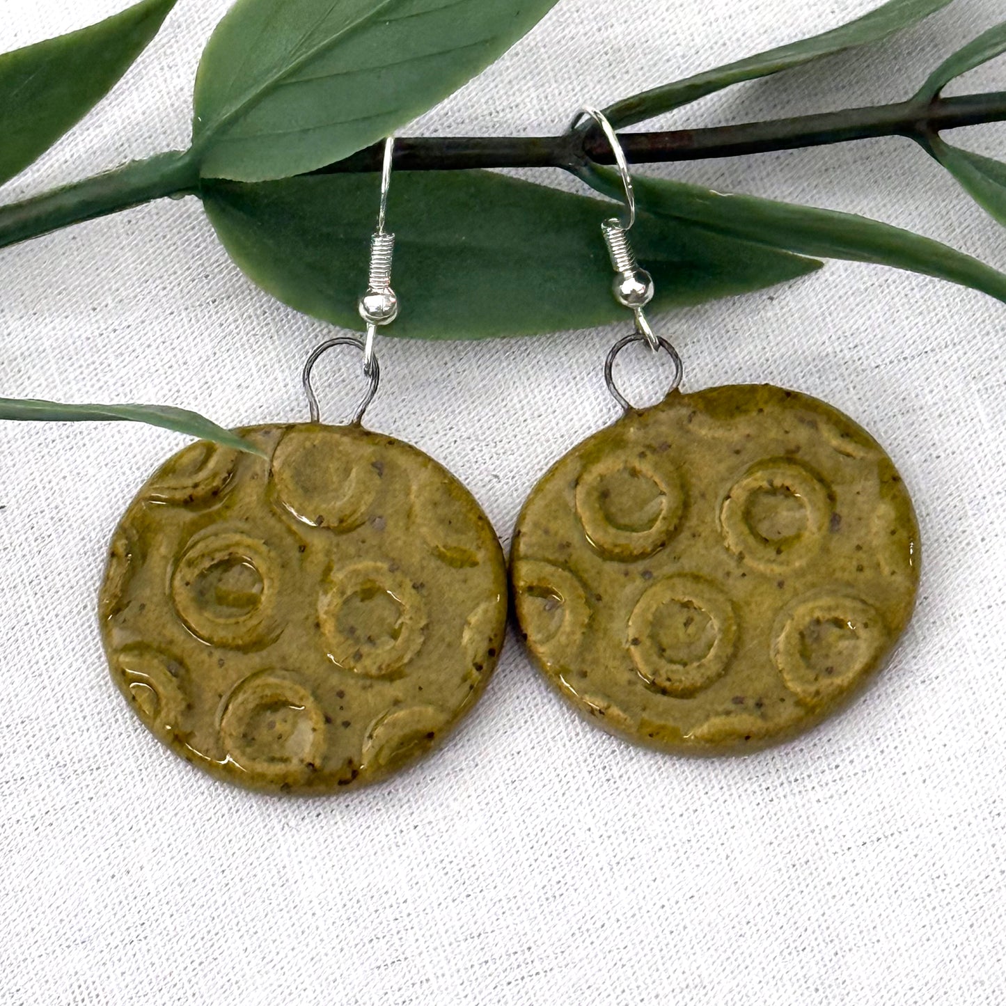 Pair of round ceramic earrings with circular patterns on a white fabric background.