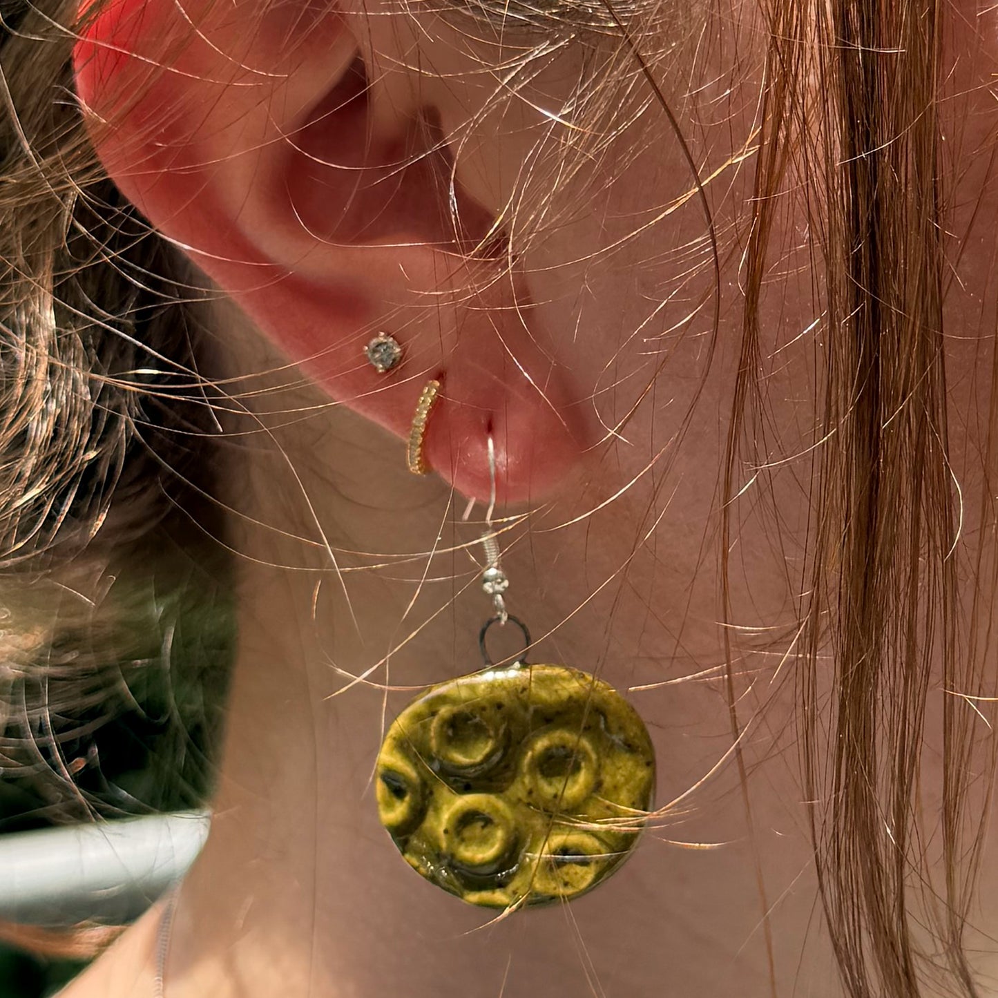 Close-up of an ear with green circular earrings.