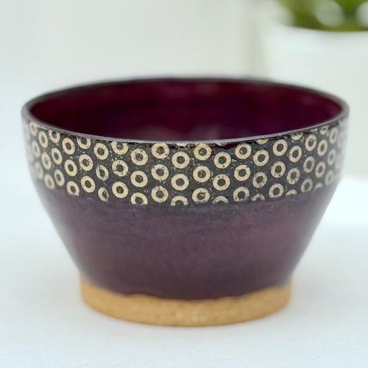 Ceramic bowl with purple glaze and circular pattern on a white background
