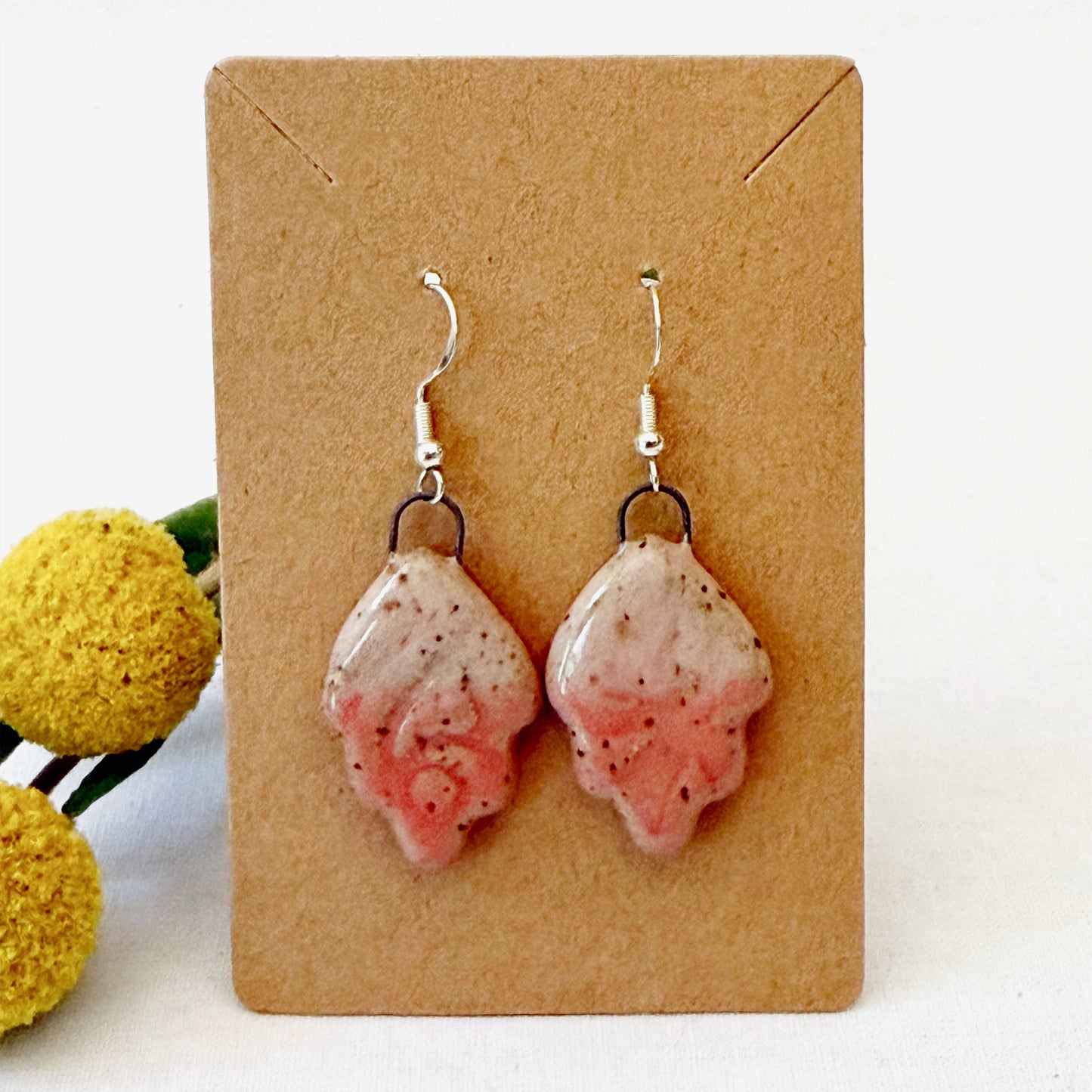 Pink speckled earrings on a brown card with yellow flowers in the background