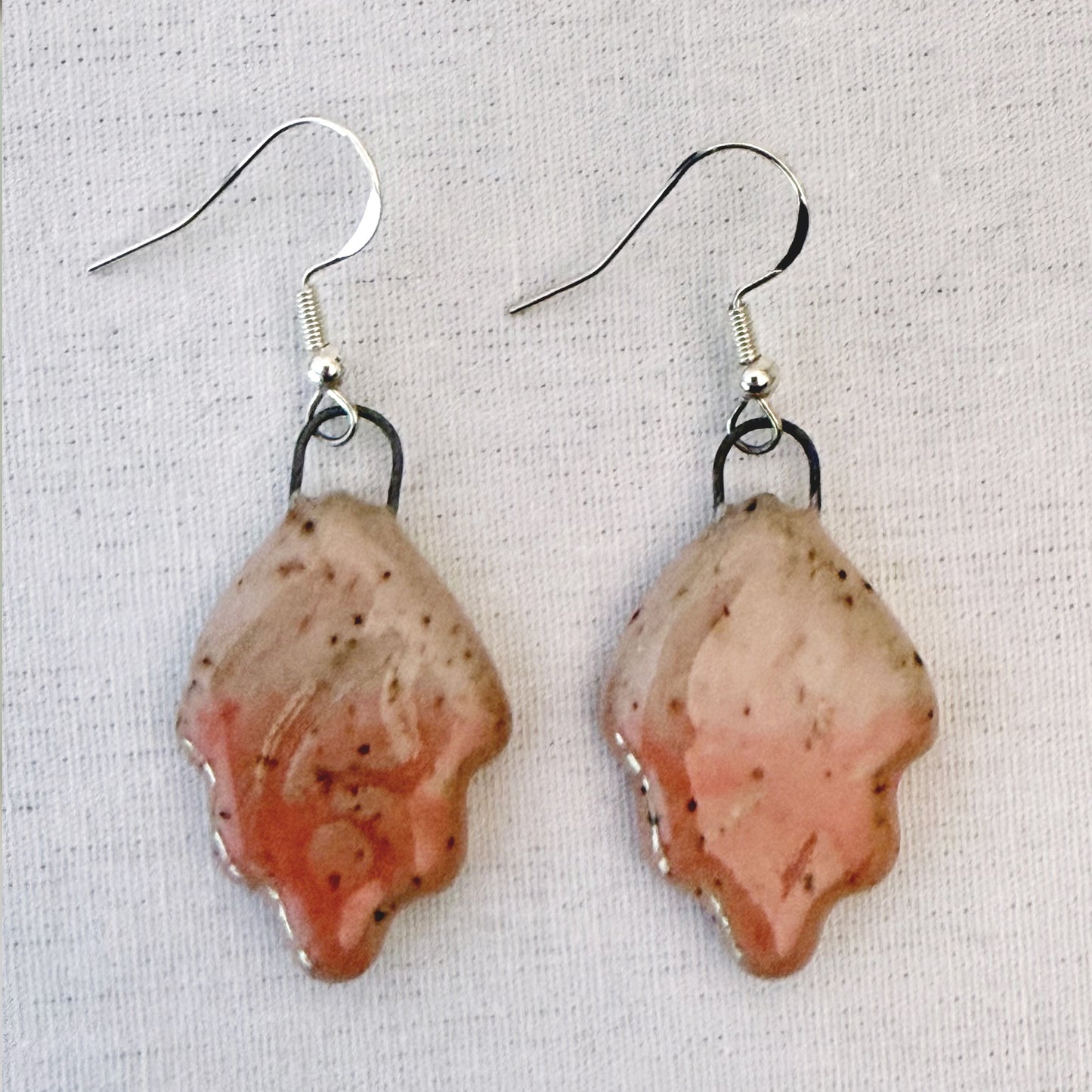 Pair of earrings with pink and brown speckled design on a light fabric background