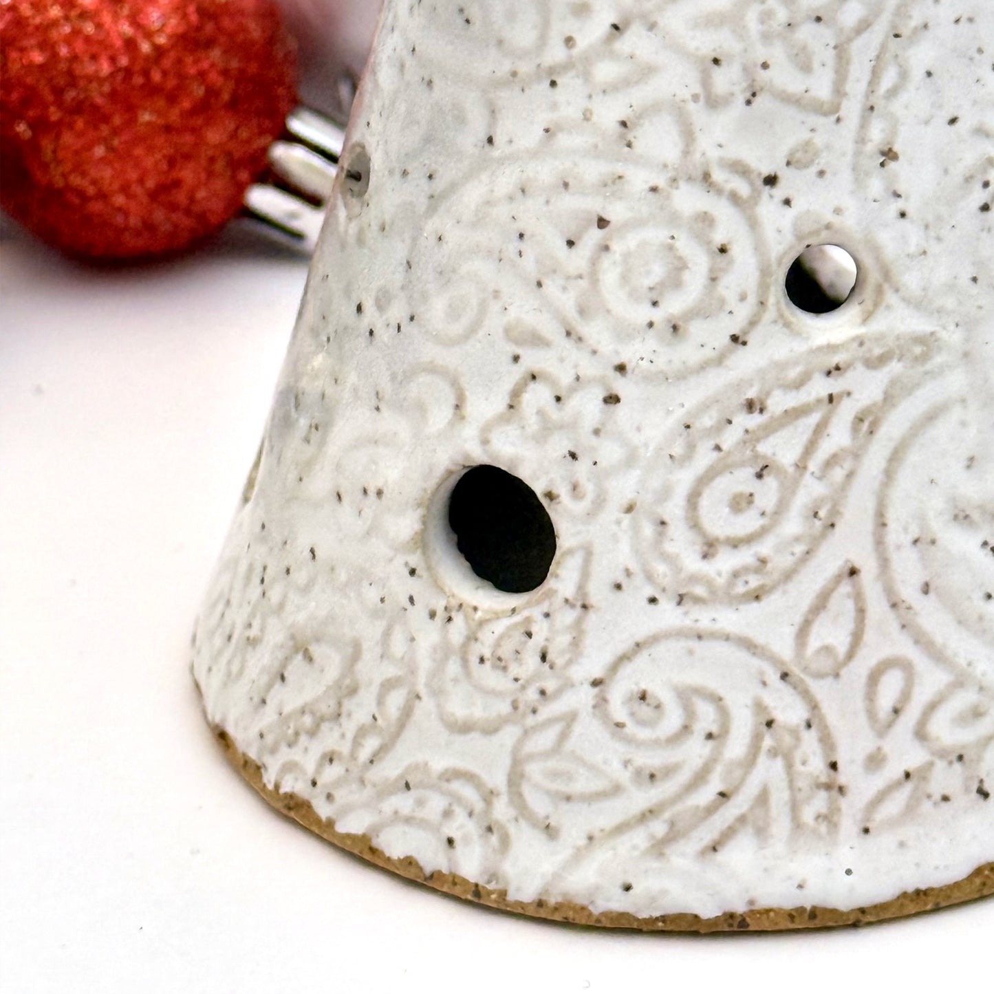 Close-up of A handcrafted white paisley-textured ceramic tree with light holes, displayed with assorted holiday ornaments.
