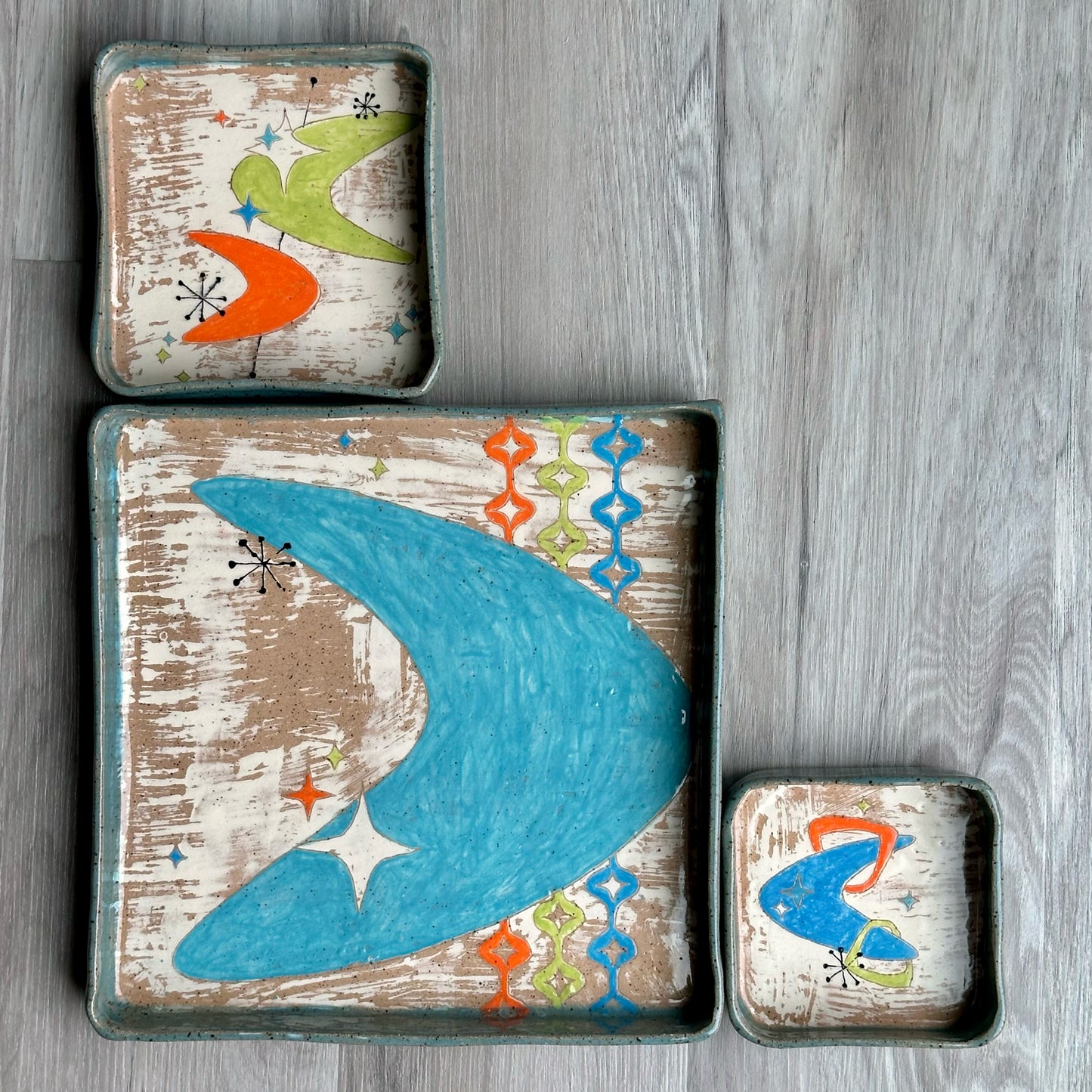 Set of three decorative trays with mid century designs on a wooden background