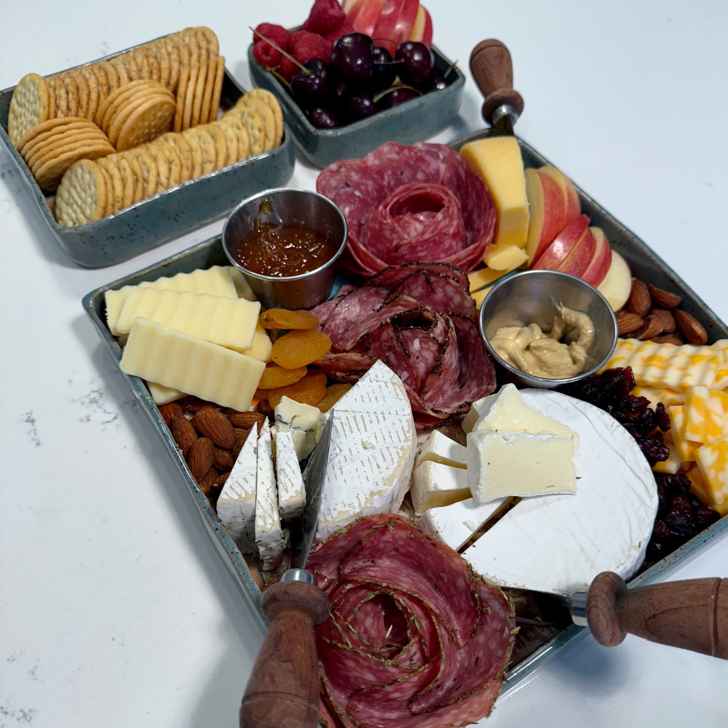Charcuterie board with meats, cheeses, fruits, and crackers on a white surface.