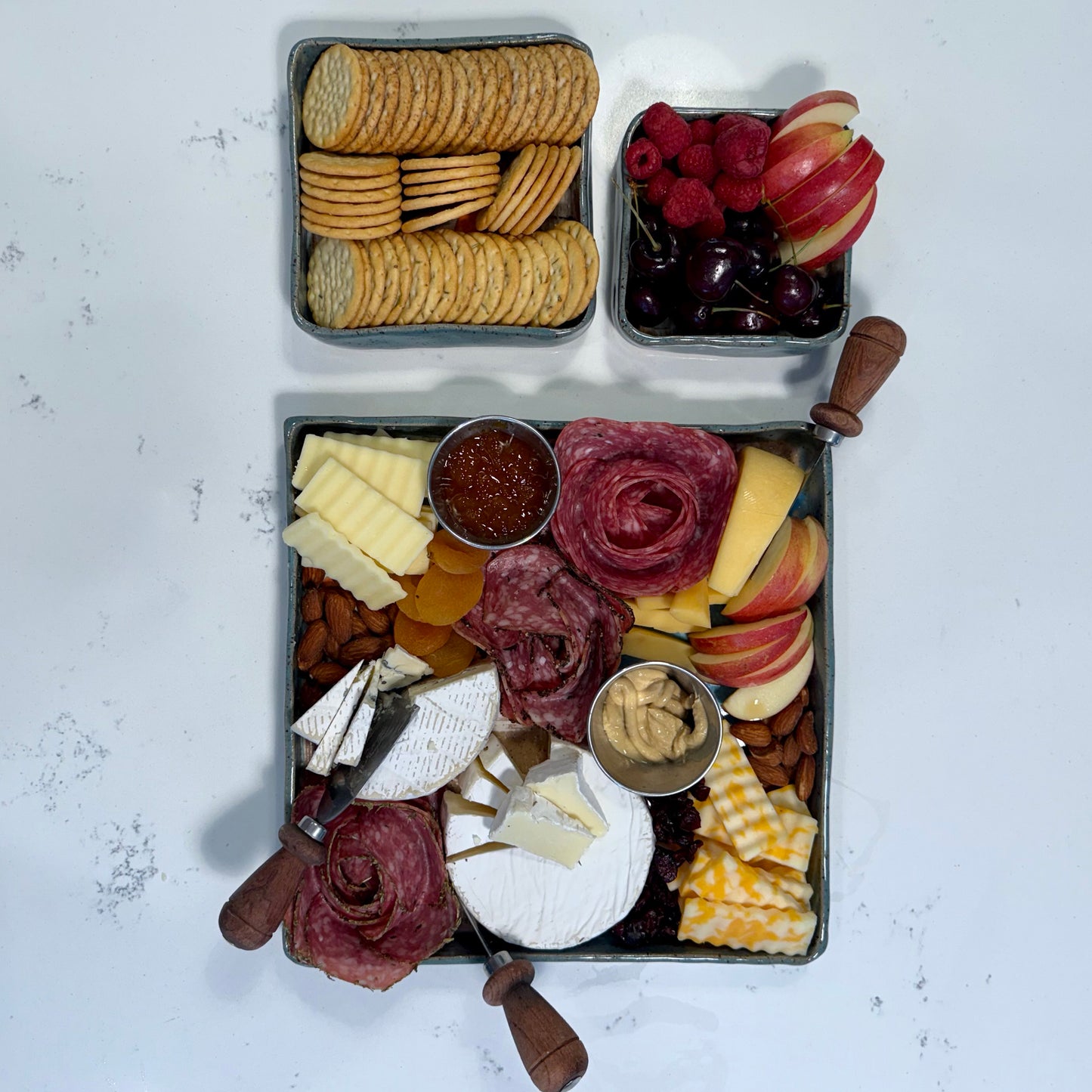 Charcuterie board with various meats, cheeses, fruits, and crackers on a white surface.